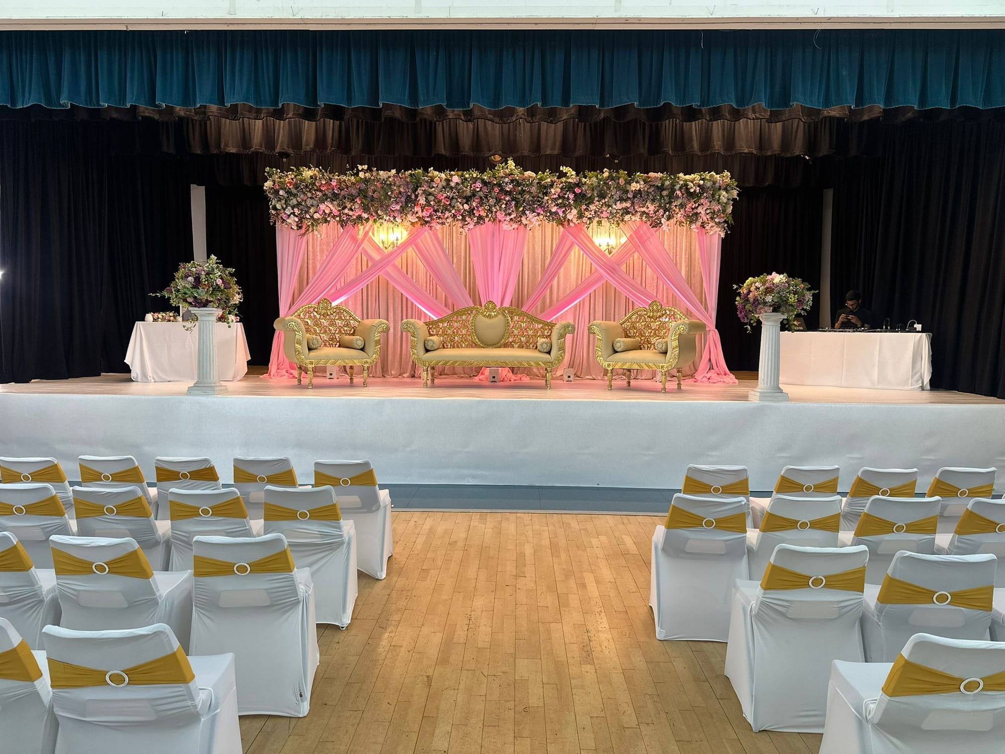 Allum Hall set for a ceremony with a pink and gold draped stage and gold chair sashes