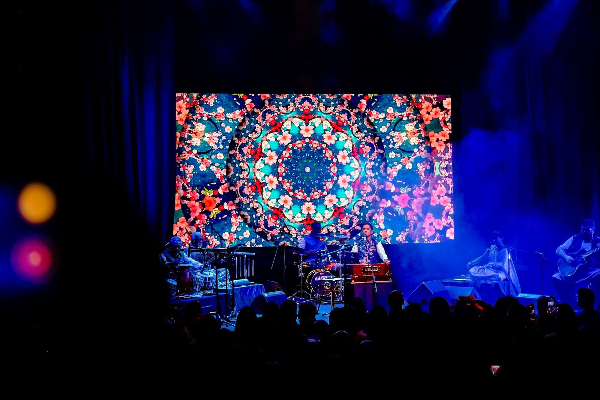 A full-width LED wall showing a kaleidoscopic pattern behind a live band