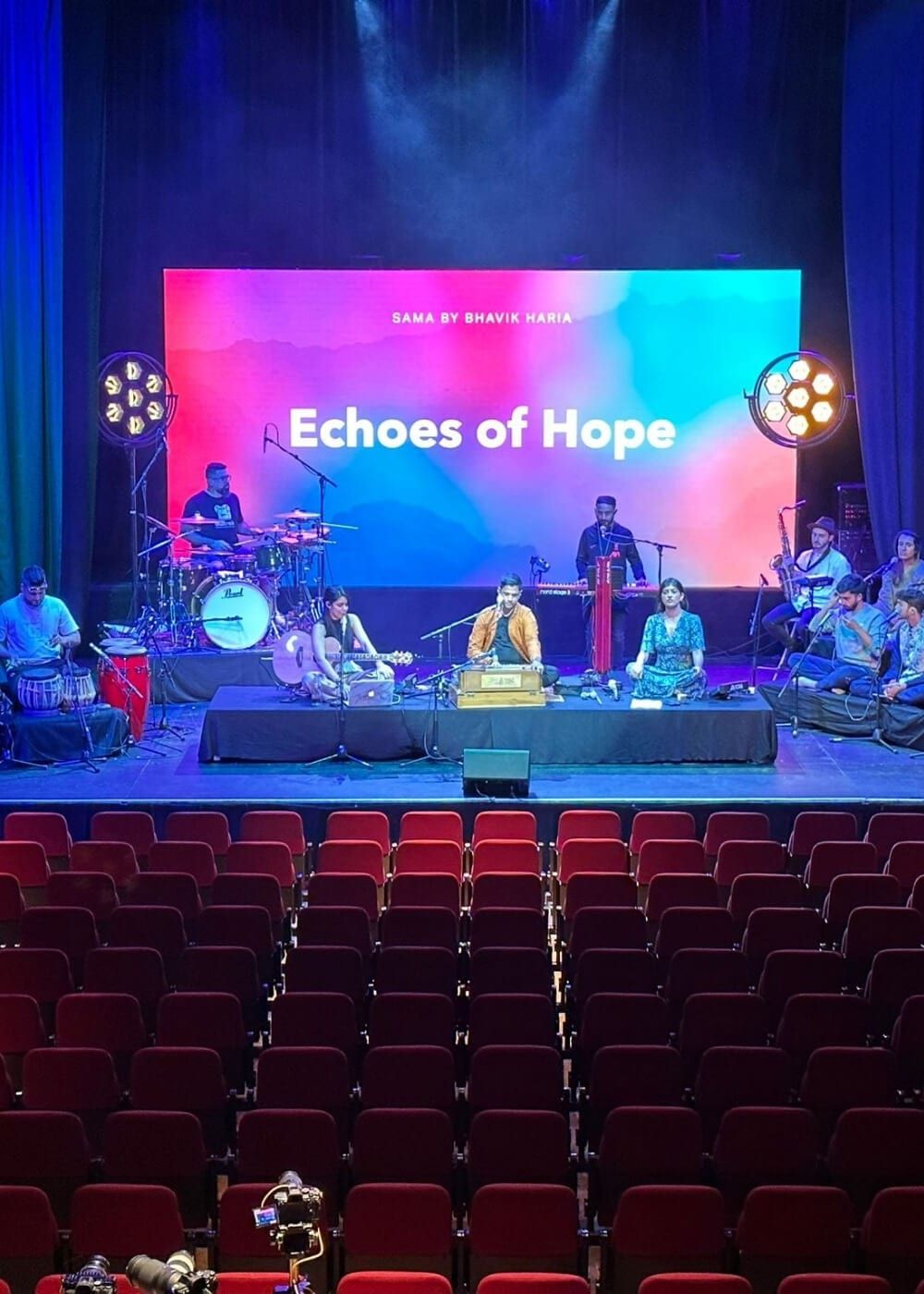 A stage under a wide LED screen with a live band in front of tiered red seating