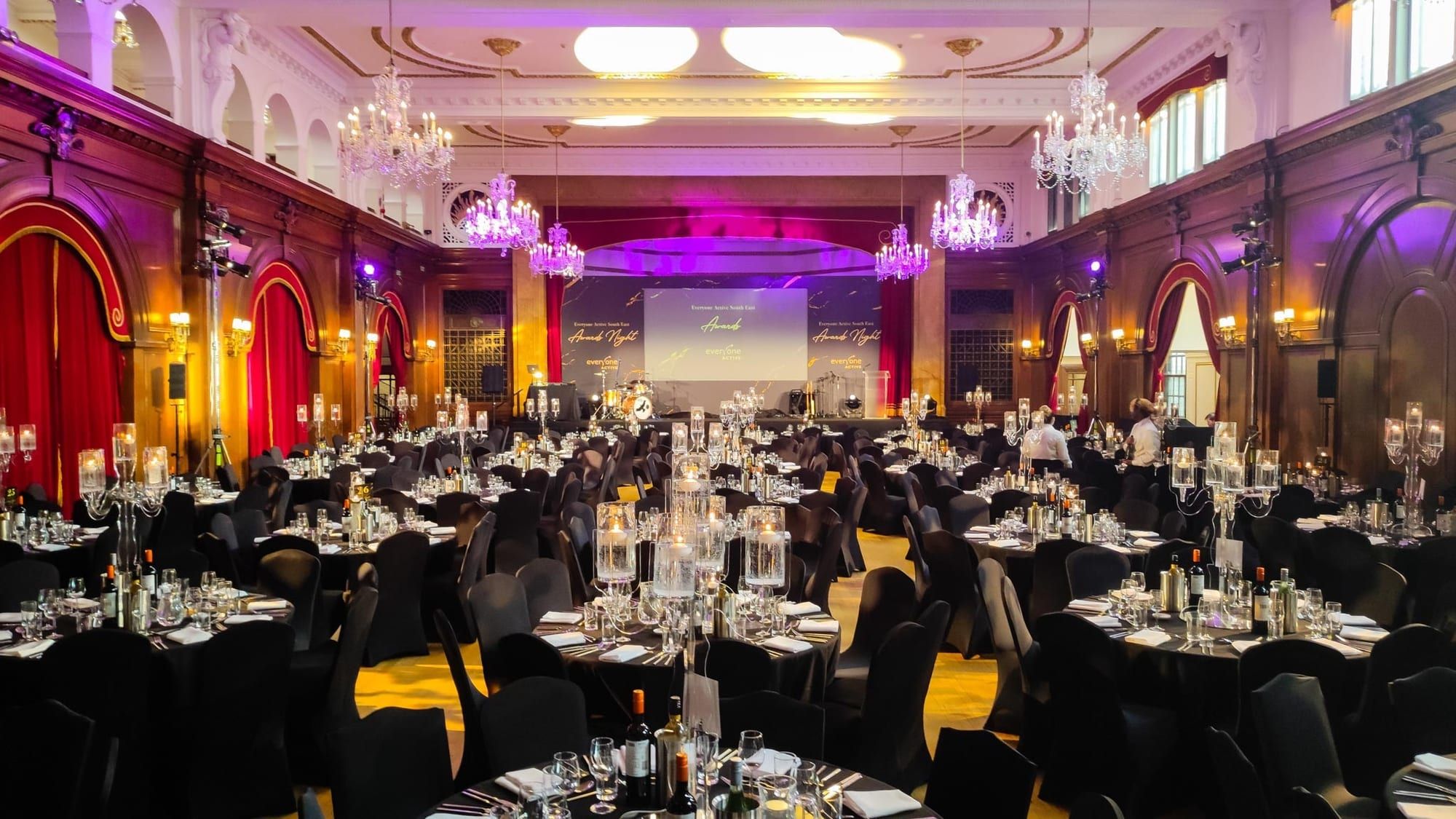 A ballroom of round tables under chandeliers, set for an awards dinner
