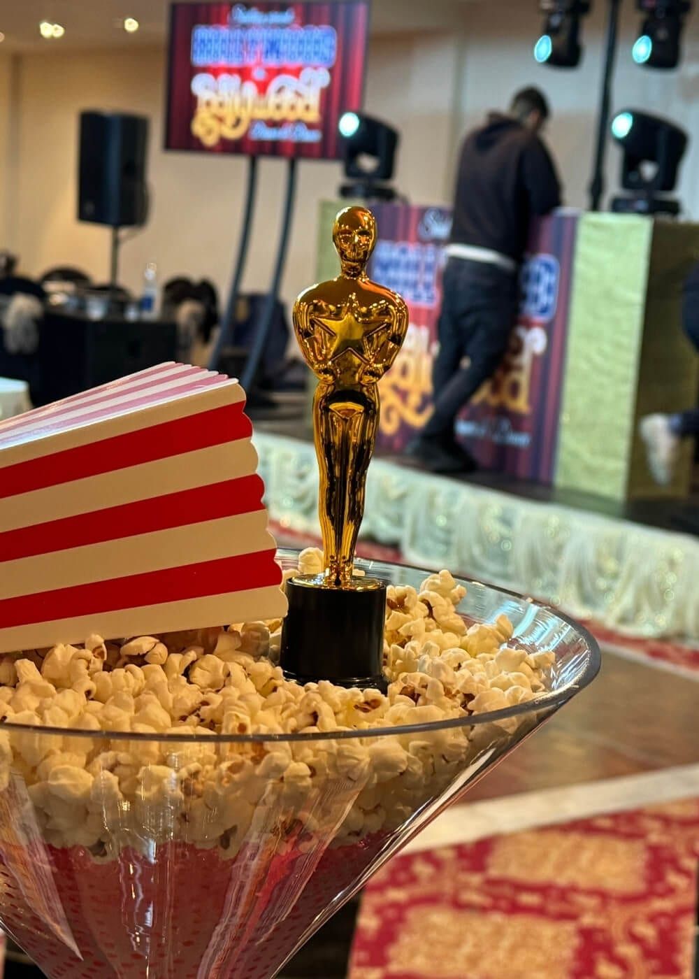 A gold statuette standing in a bowl of popcorn beside a striped carton