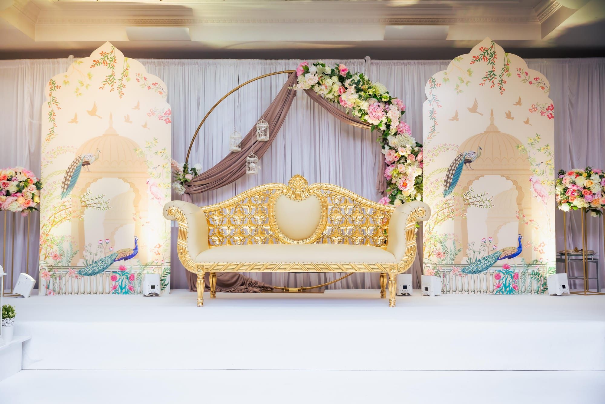 A cream and gold stage set with a circular floral arch behind a carved sofa