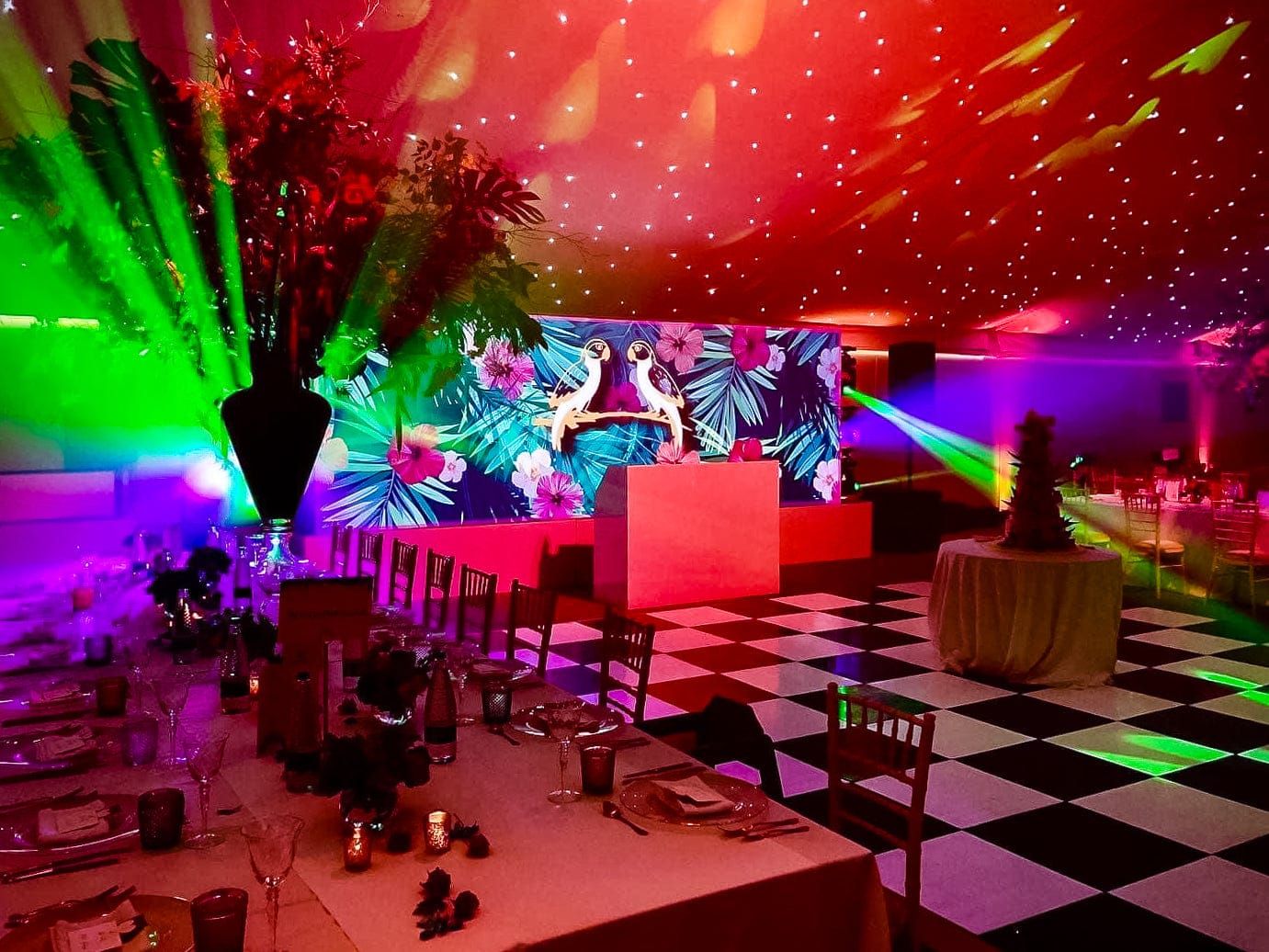 A party room lit in green and pink with a tropical print backdrop and a chequered floor