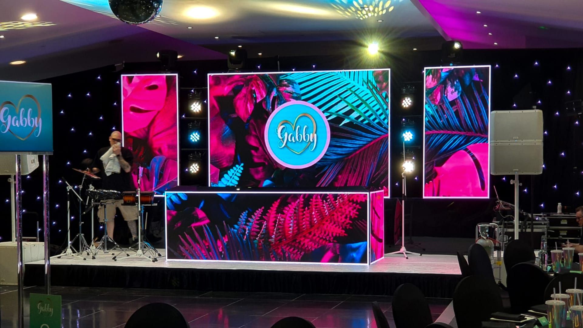 A stage set with a printed tropical screen and a live drummer