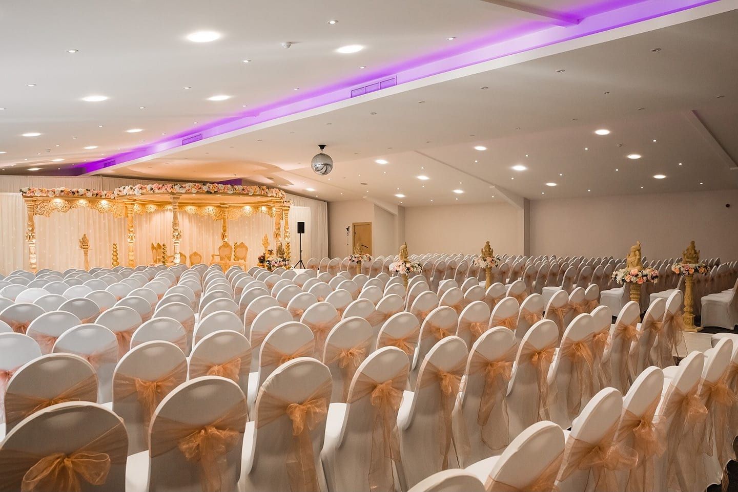 Rows of white covered chairs with gold organza sashes filling a ballroom