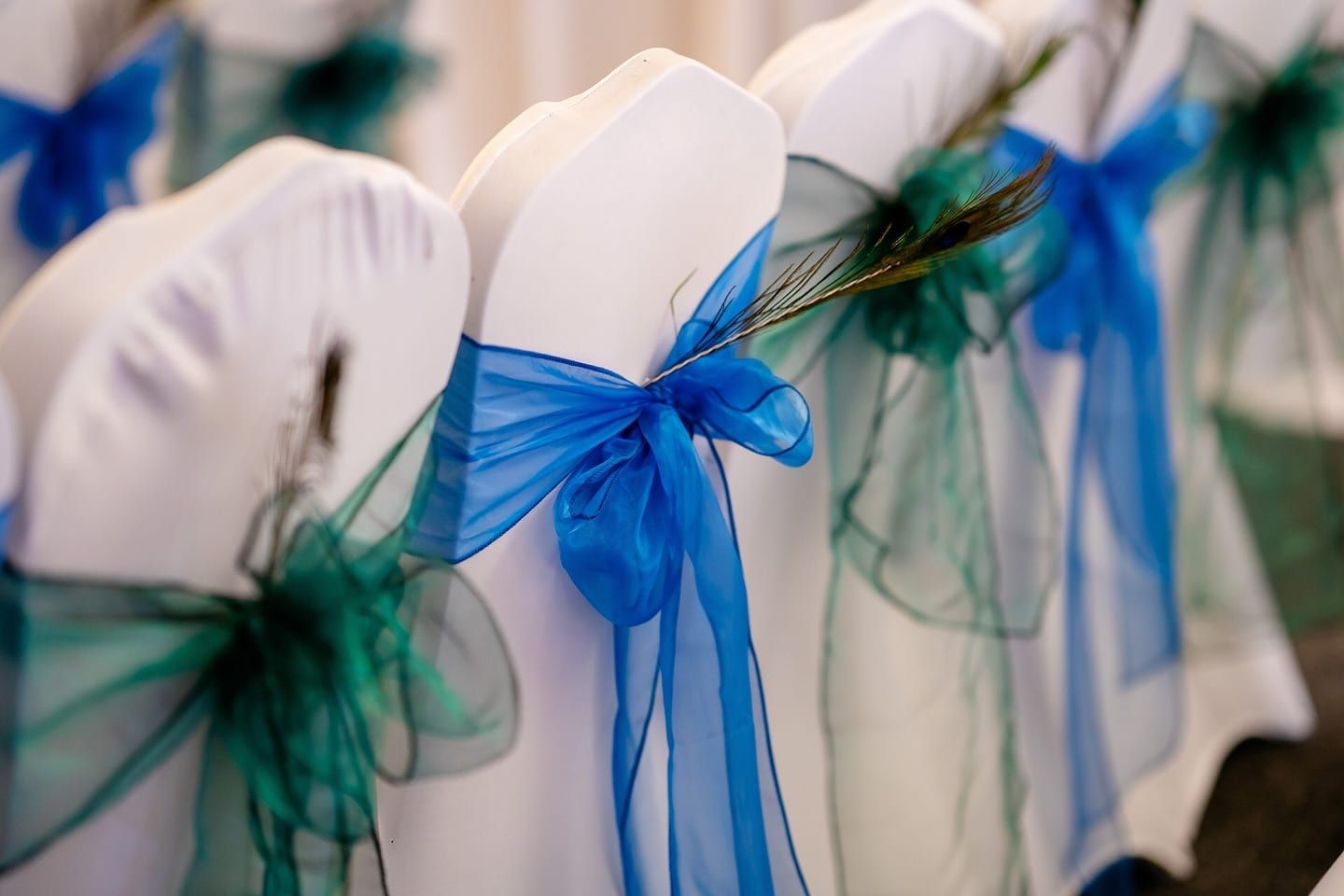 White chair covers finished with teal organza bows and a peacock feather detail
