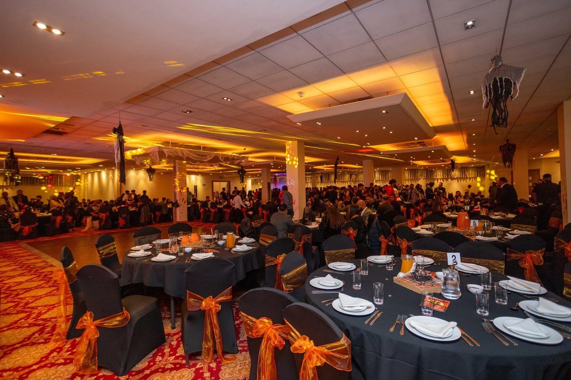 A charity dinner filling a banqueting hall, tables dressed with orange sashes