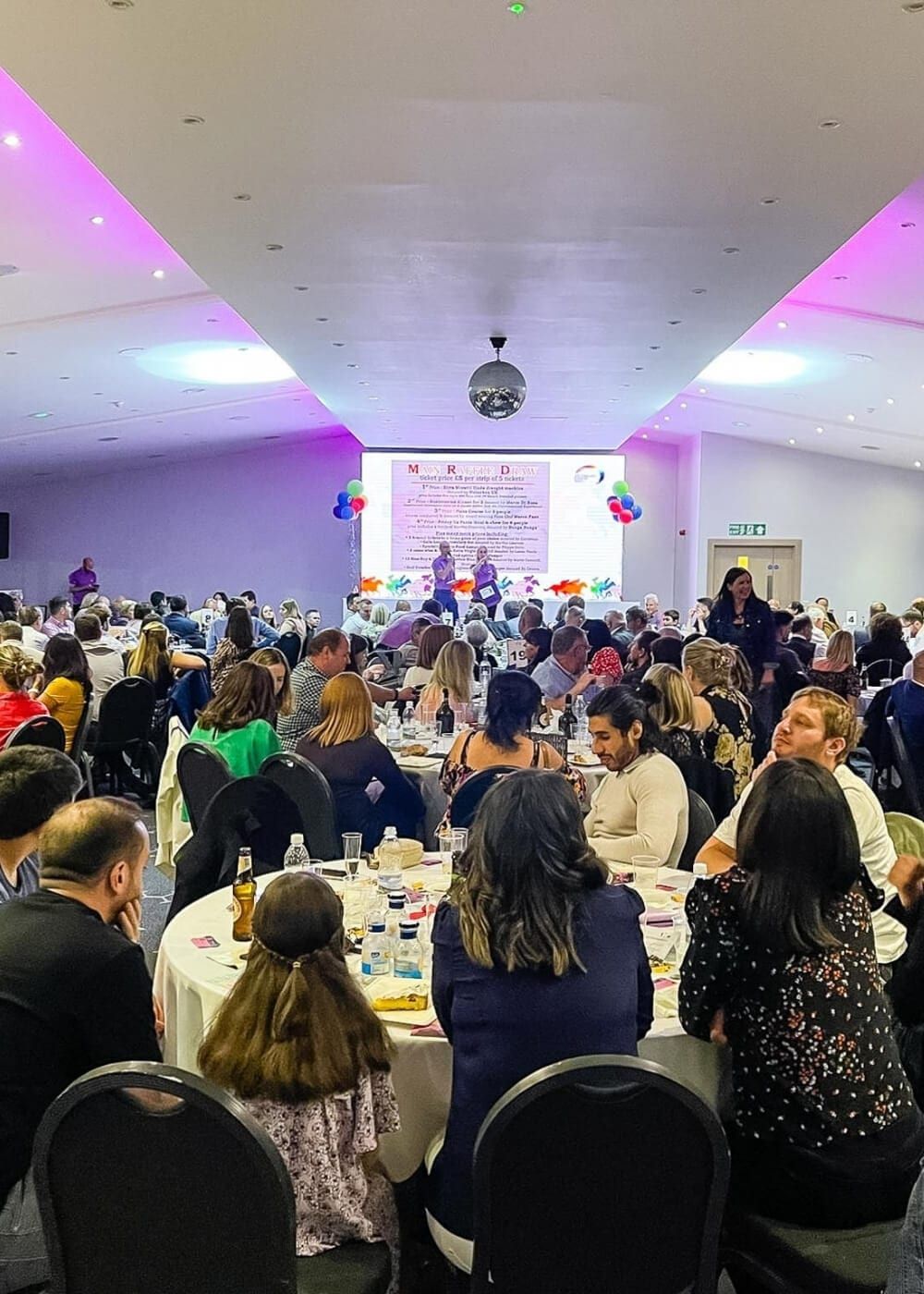 A hall of guests at round tables during a charity fundraiser