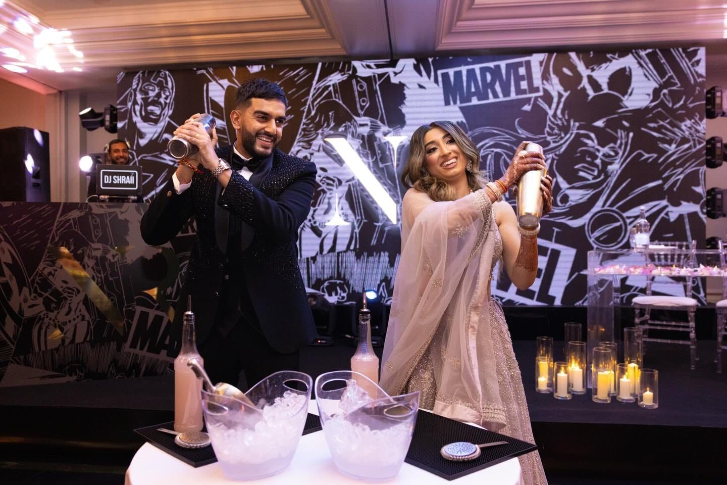 The couple shaking cocktails together in front of a comic-book LED backdrop