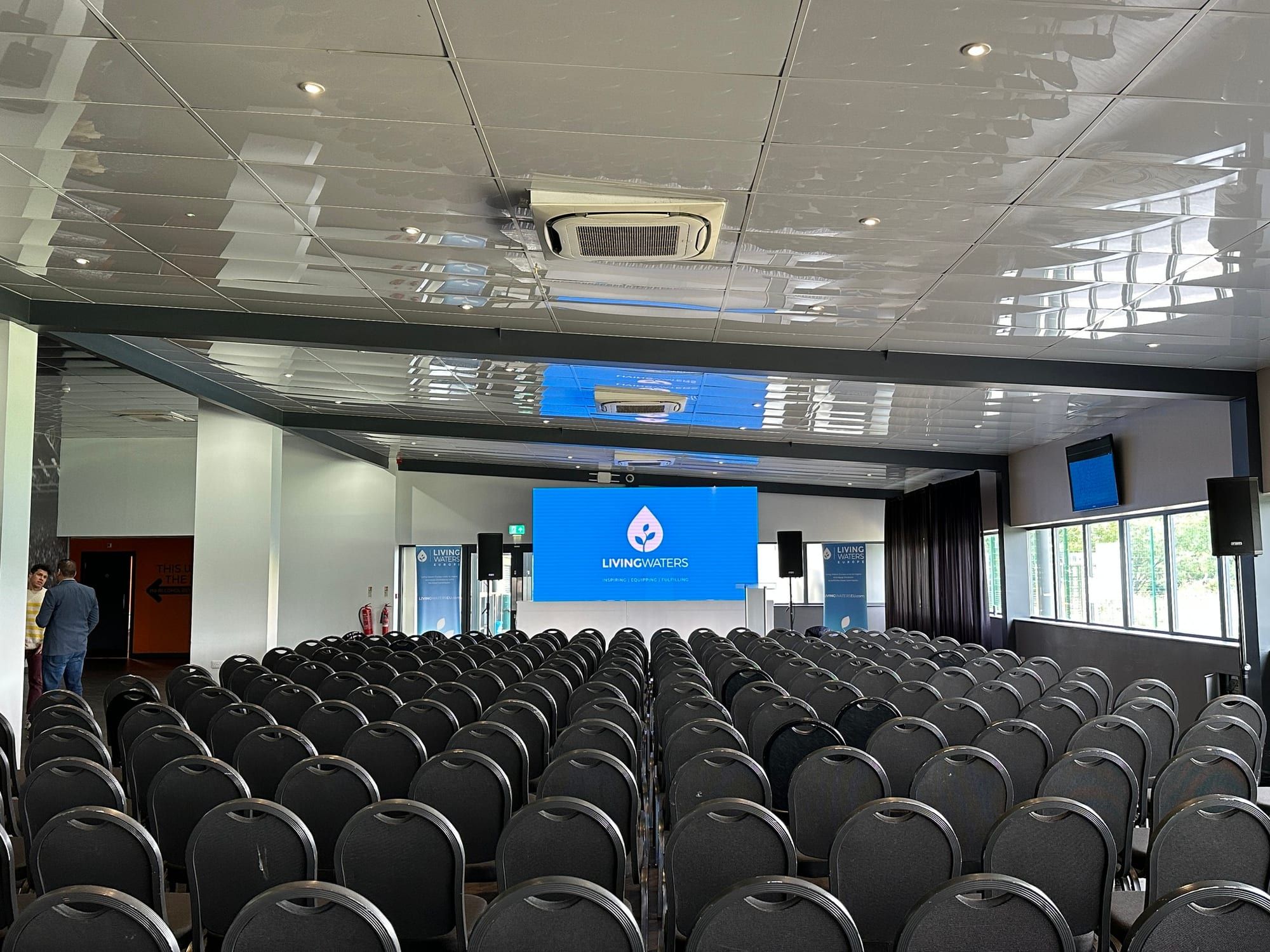 Rows of black conference chairs facing a lit presentation screen
