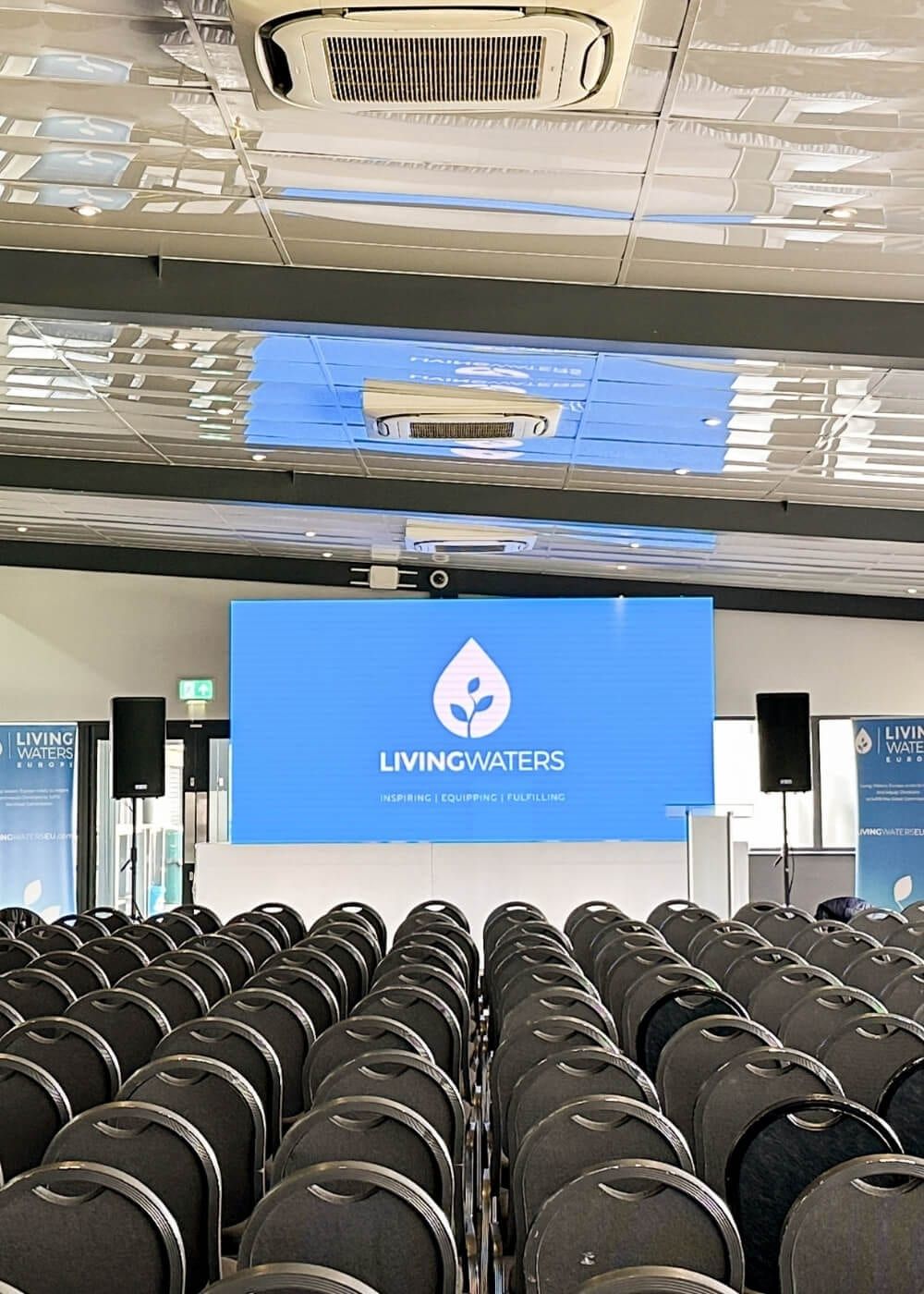 A branded screen and speakers set up in front of seated rows
