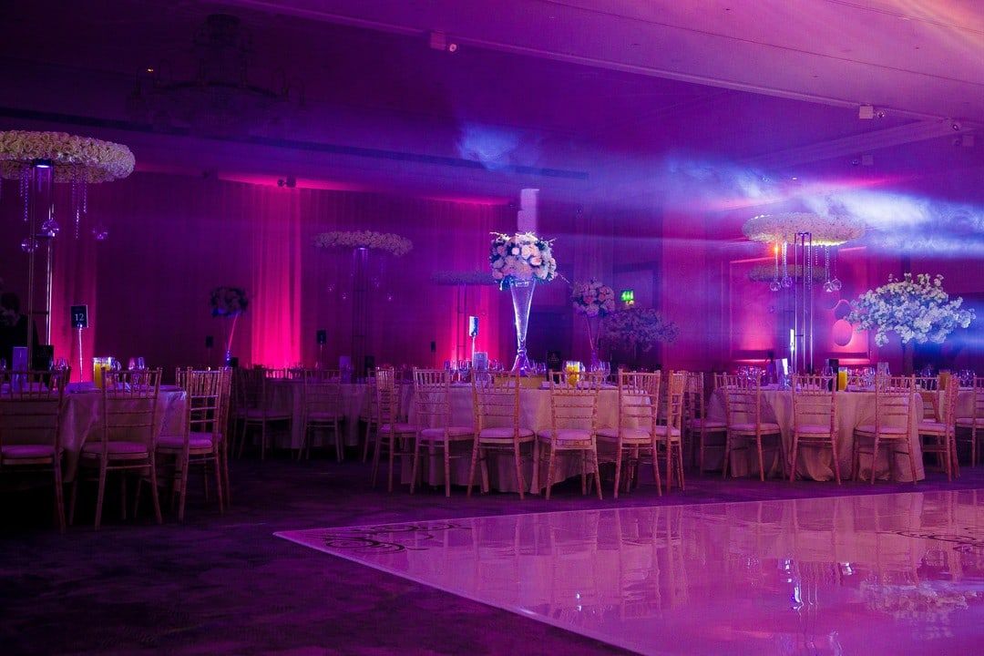 A ballroom washed magenta and violet, laid tables reflected in a mirrored floor