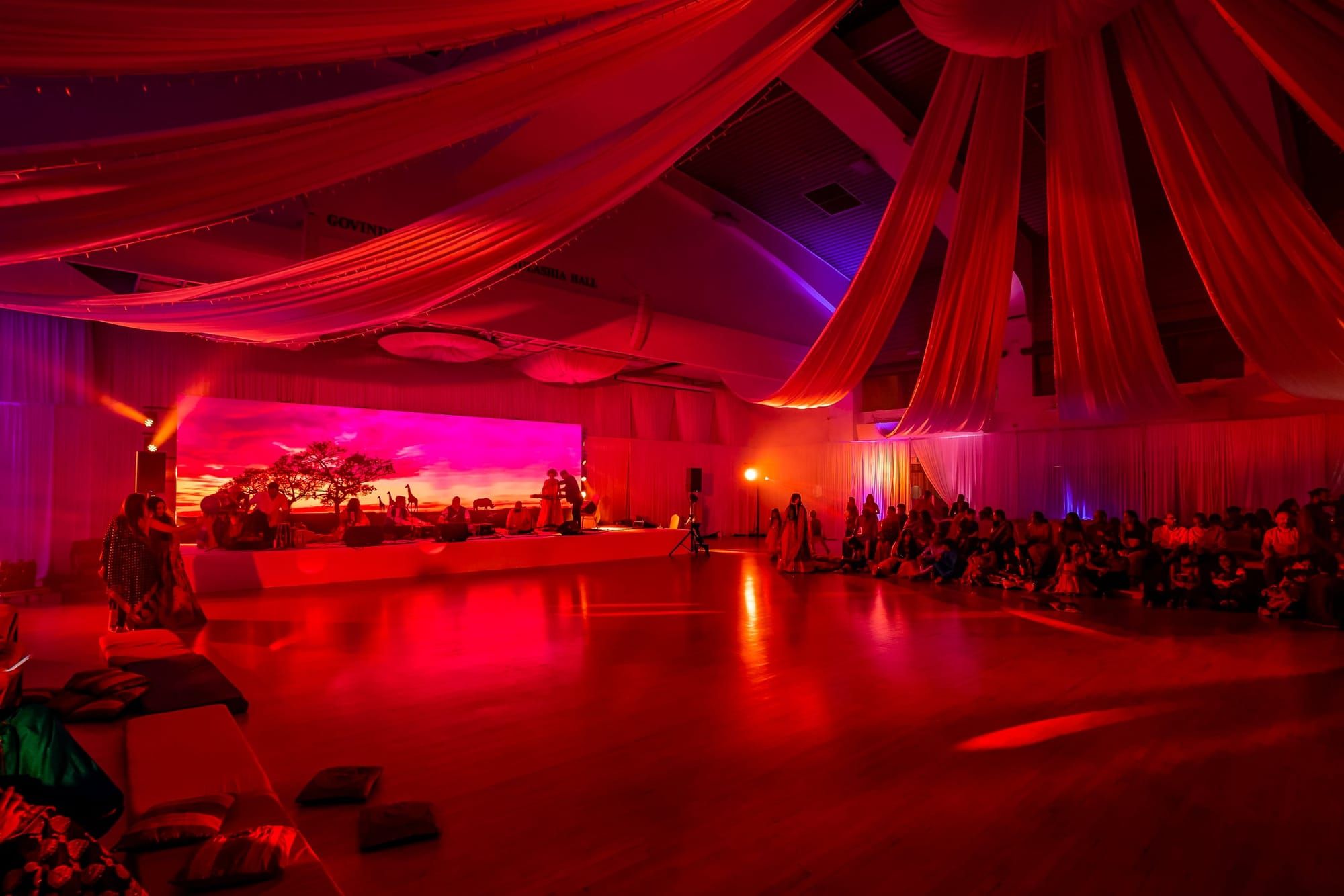 A hall draped in red with warm uplighting and a low stage