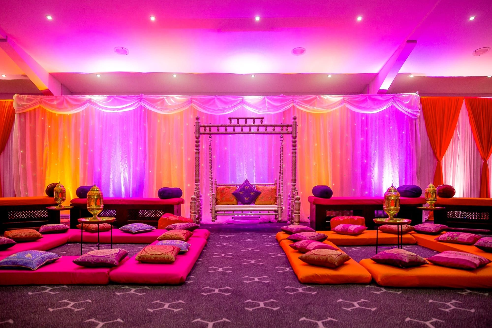 A mehndi room in pink and orange with low seating and bolster cushions