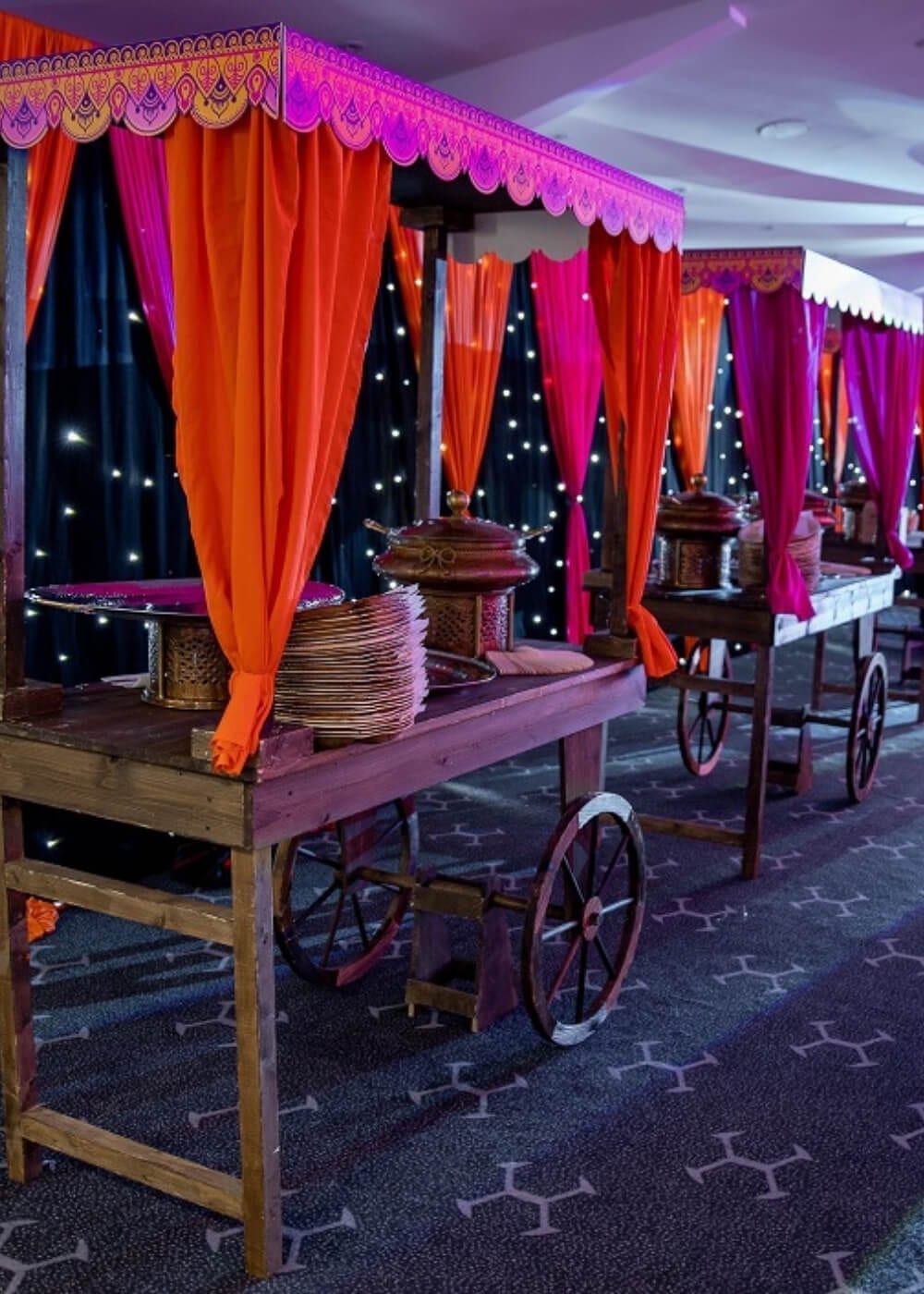 A wooden cart of copper serving pots framed by orange and gold drapes