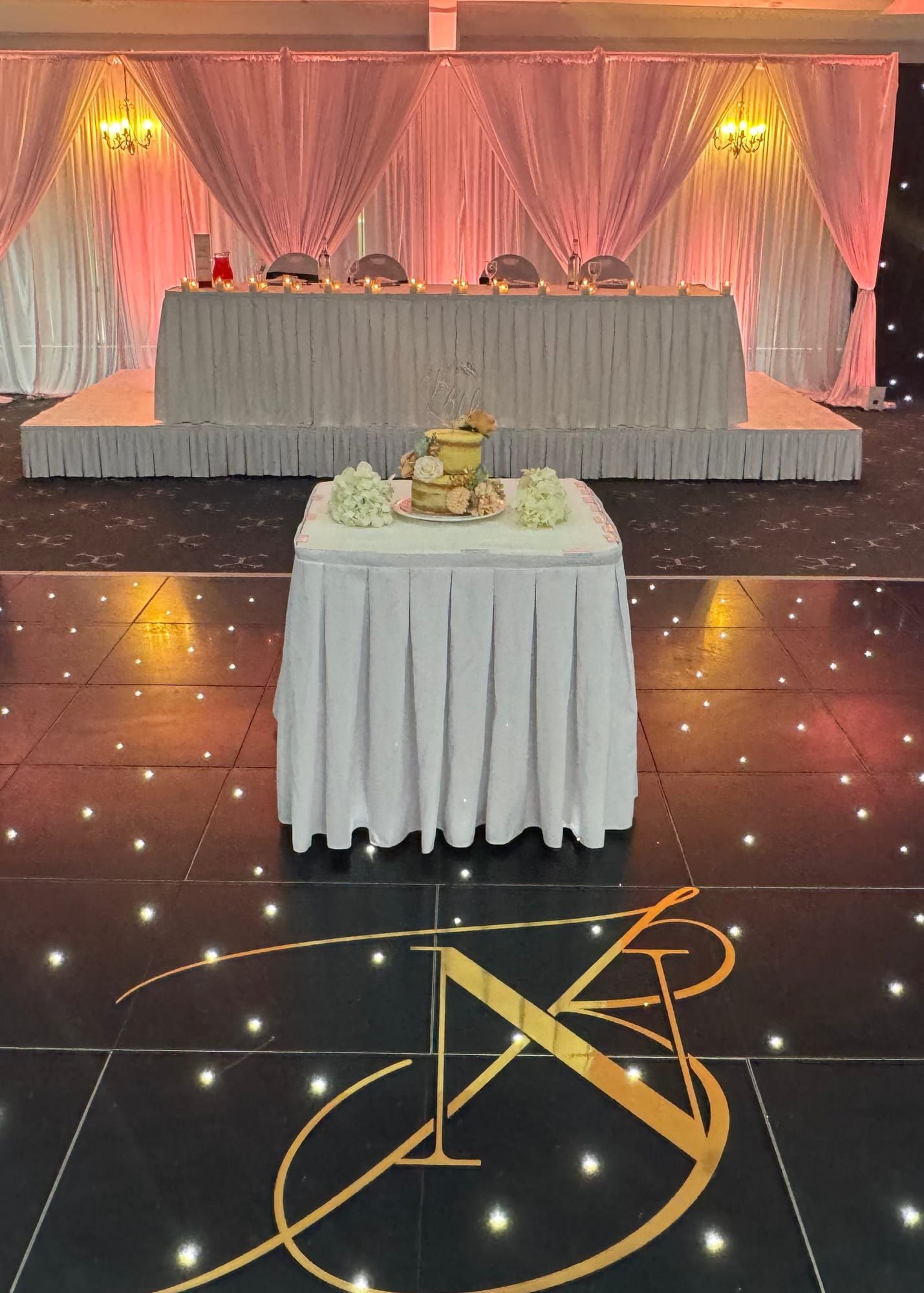 A black starlit dancefloor in front of a draped top table and cake
