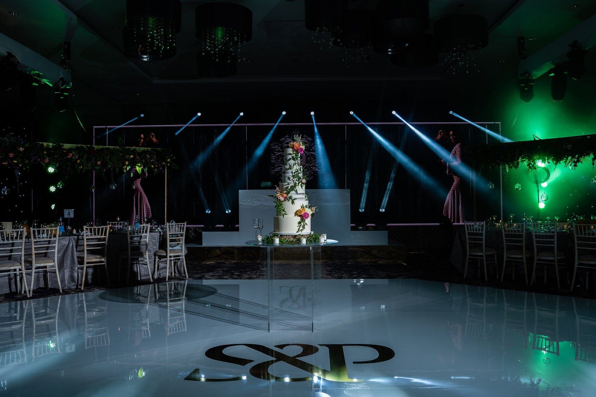 A white mirrored dancefloor carrying a monogram, ringed by uplit tables