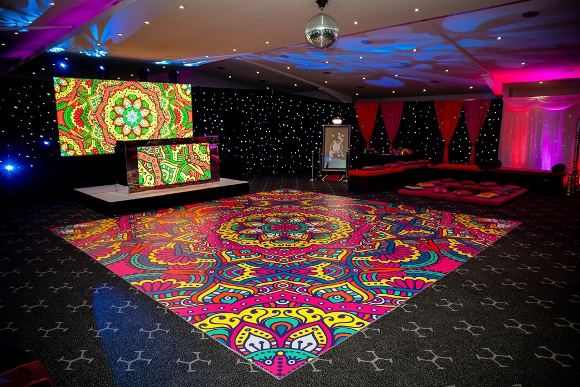 A printed mandala dancefloor in vivid colour beneath a starcloth and LED screens