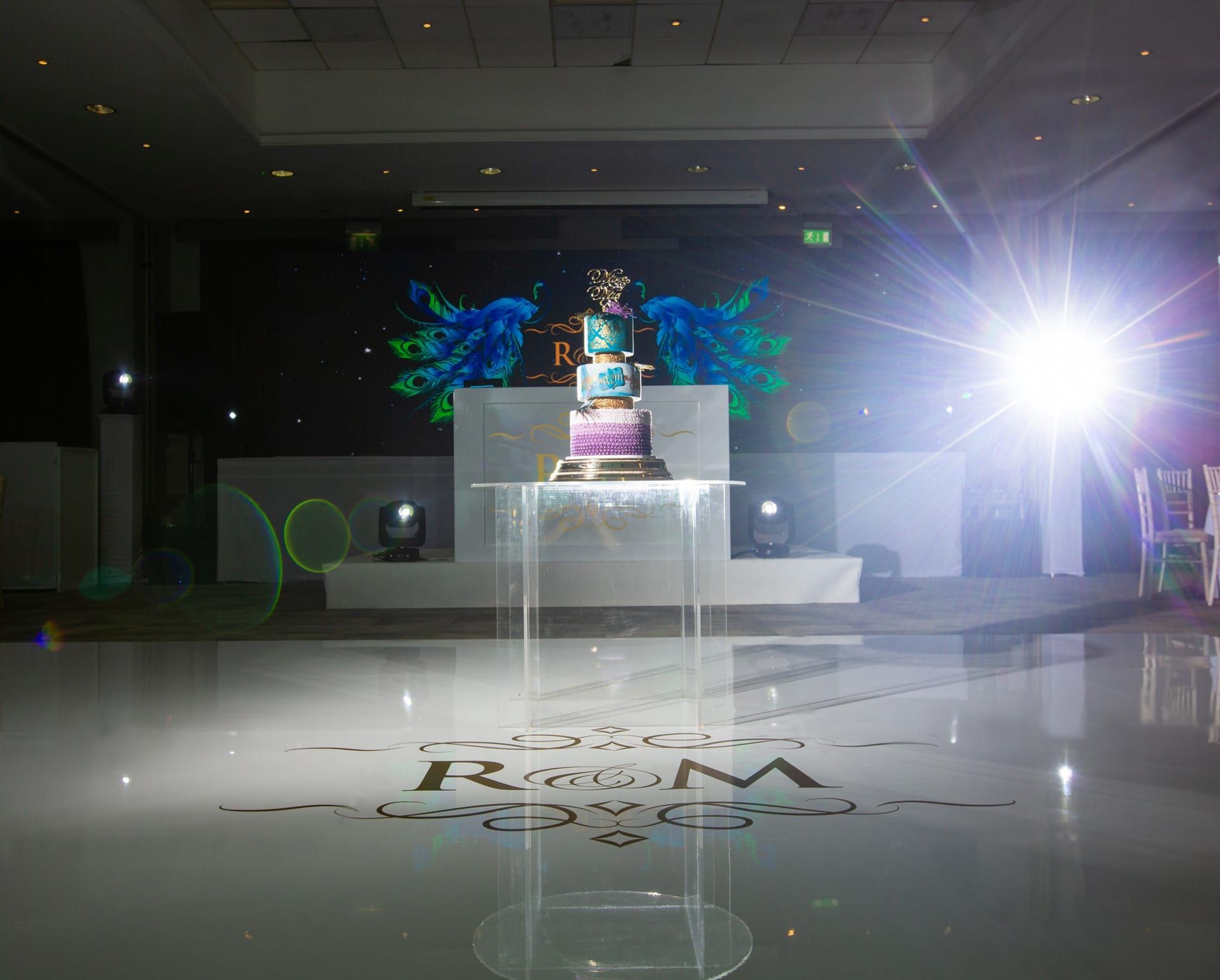 A mirrored dancefloor reflecting a lit cake table and feather displays