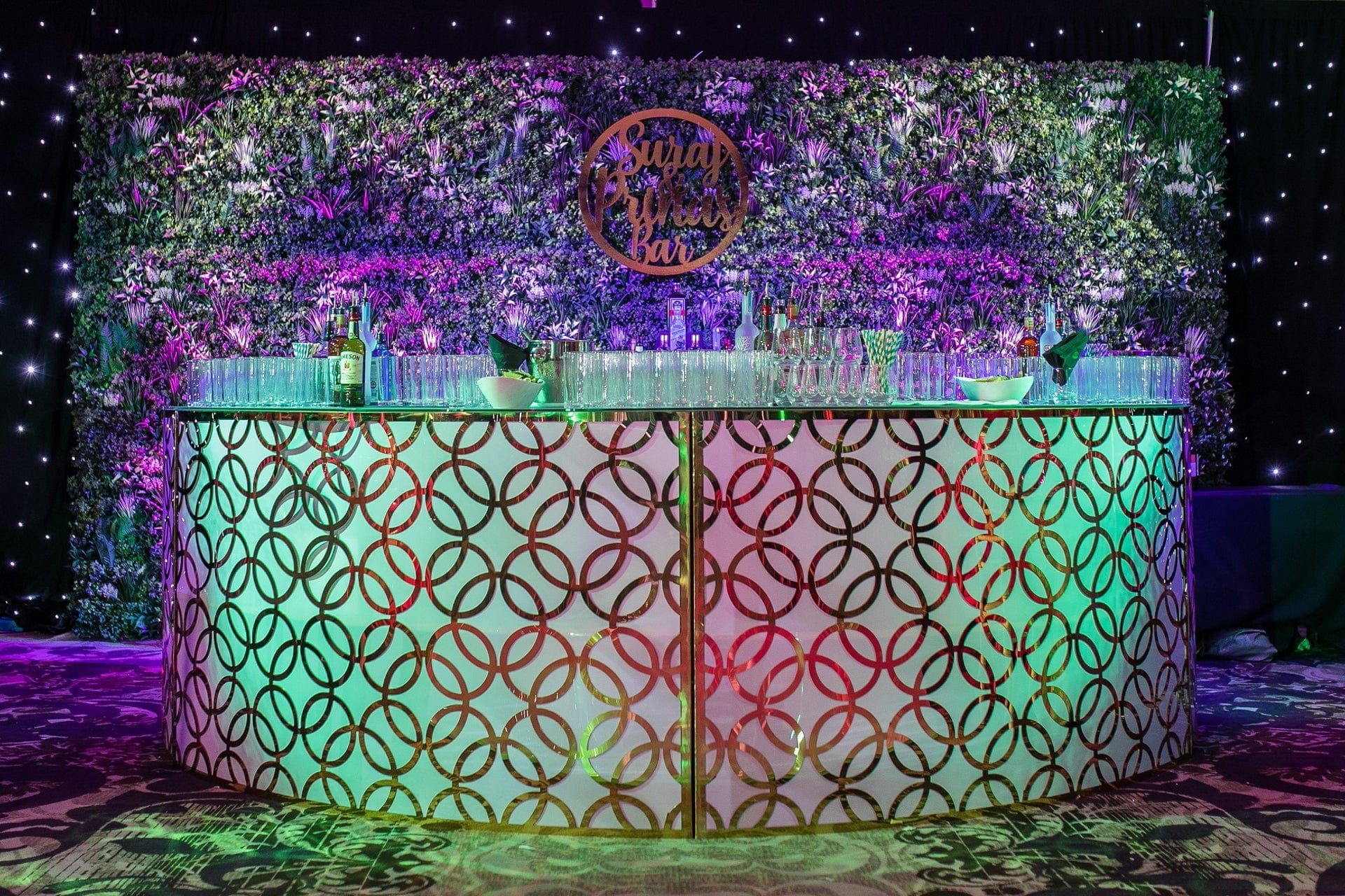 An illuminated bar front cut in a repeating pattern, backed by a floral wall