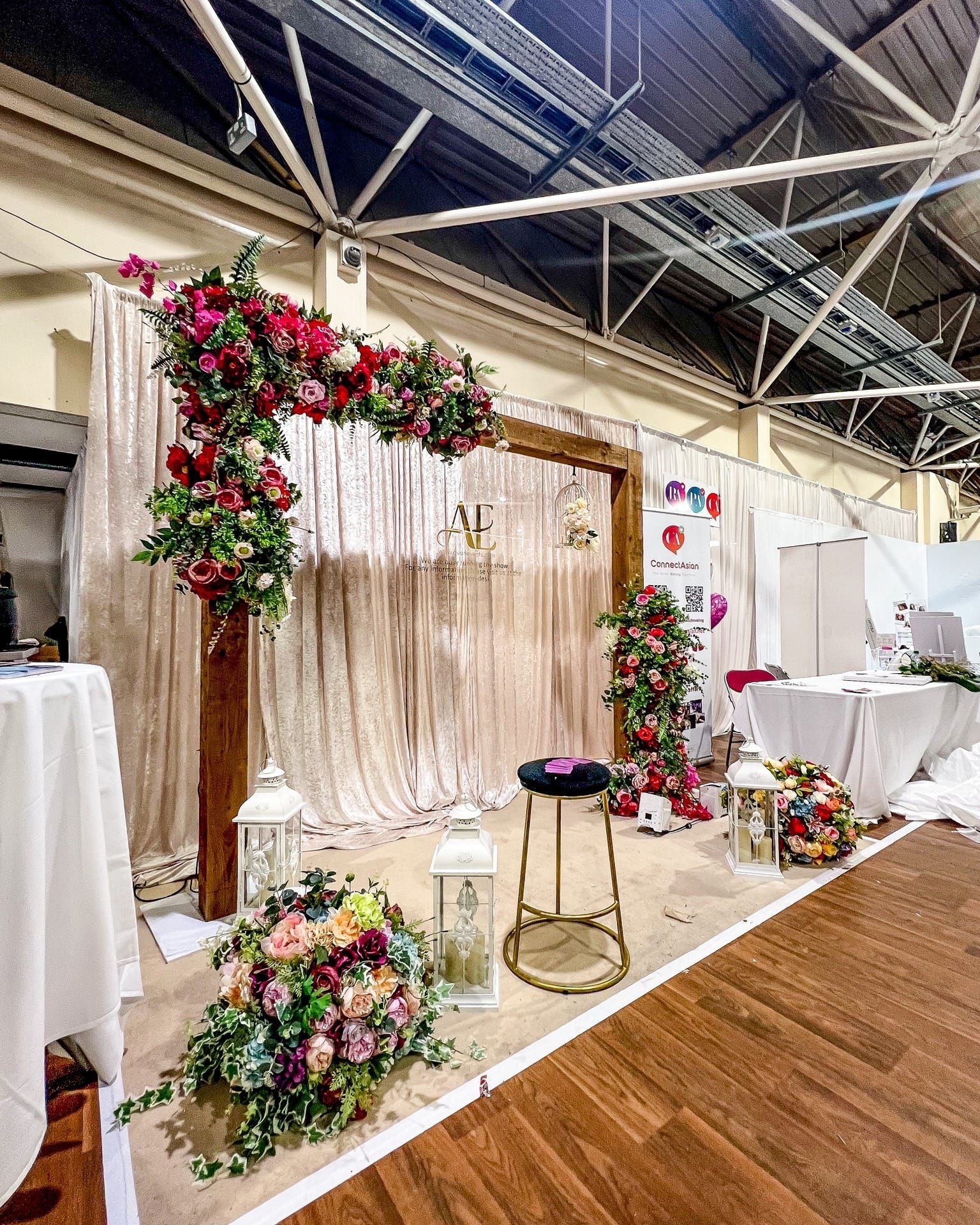 An exhibition stand dressed with a floral arch and draped walls