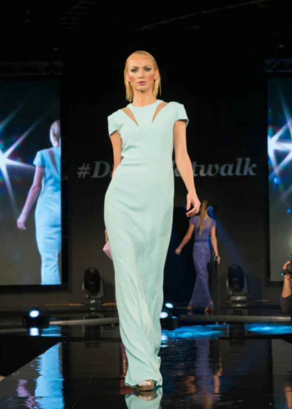 A model on the runway before a screen carrying the show's hashtag