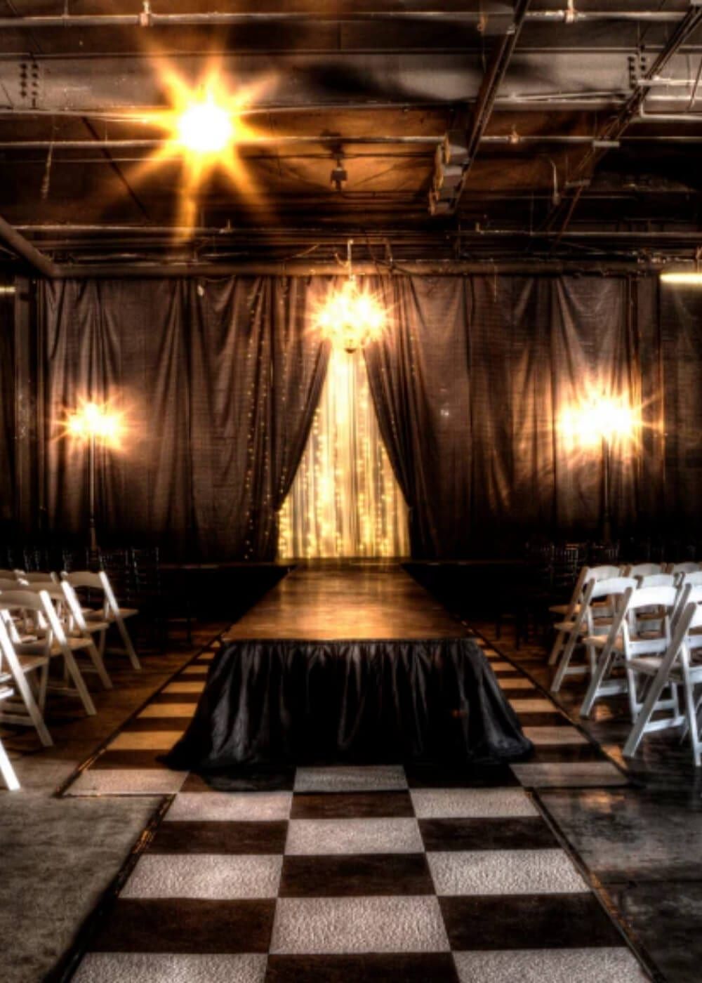 A runway laid between rows of white chairs, gold light on the curtain behind
