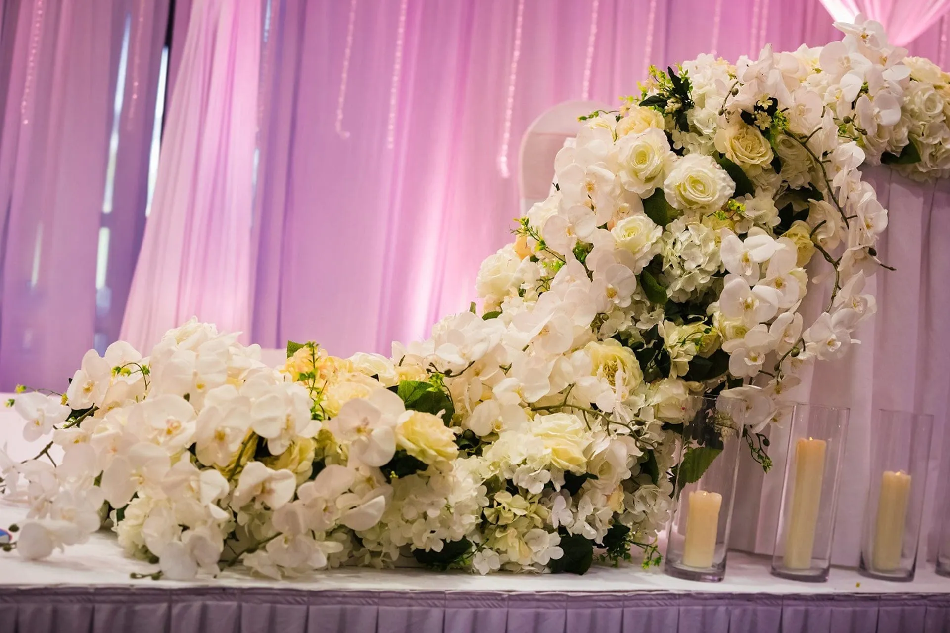 A close cascade of white roses and orchids along a stage edge