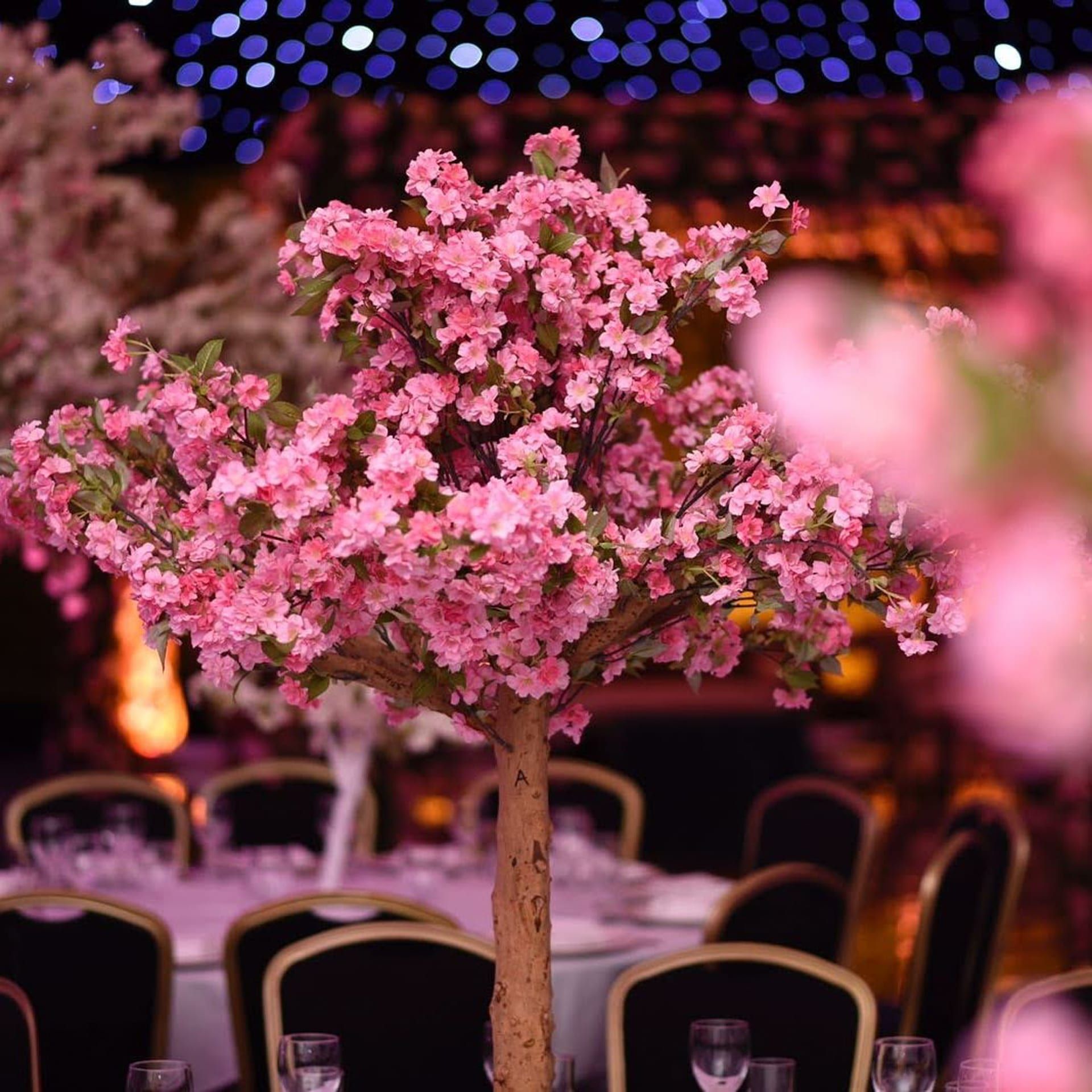 A pink blossom tree centrepiece rising over a candlelit round table