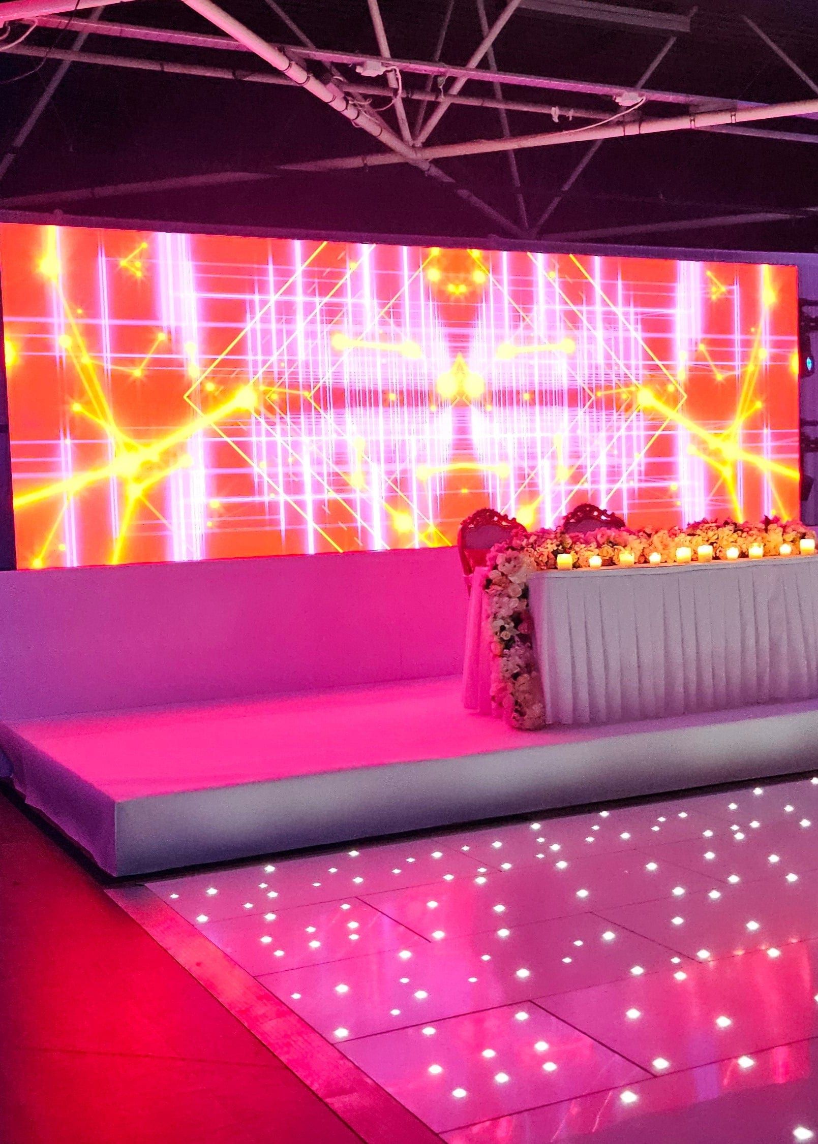 A full-width LED wall in pink and orange behind a long floral-topped sofa