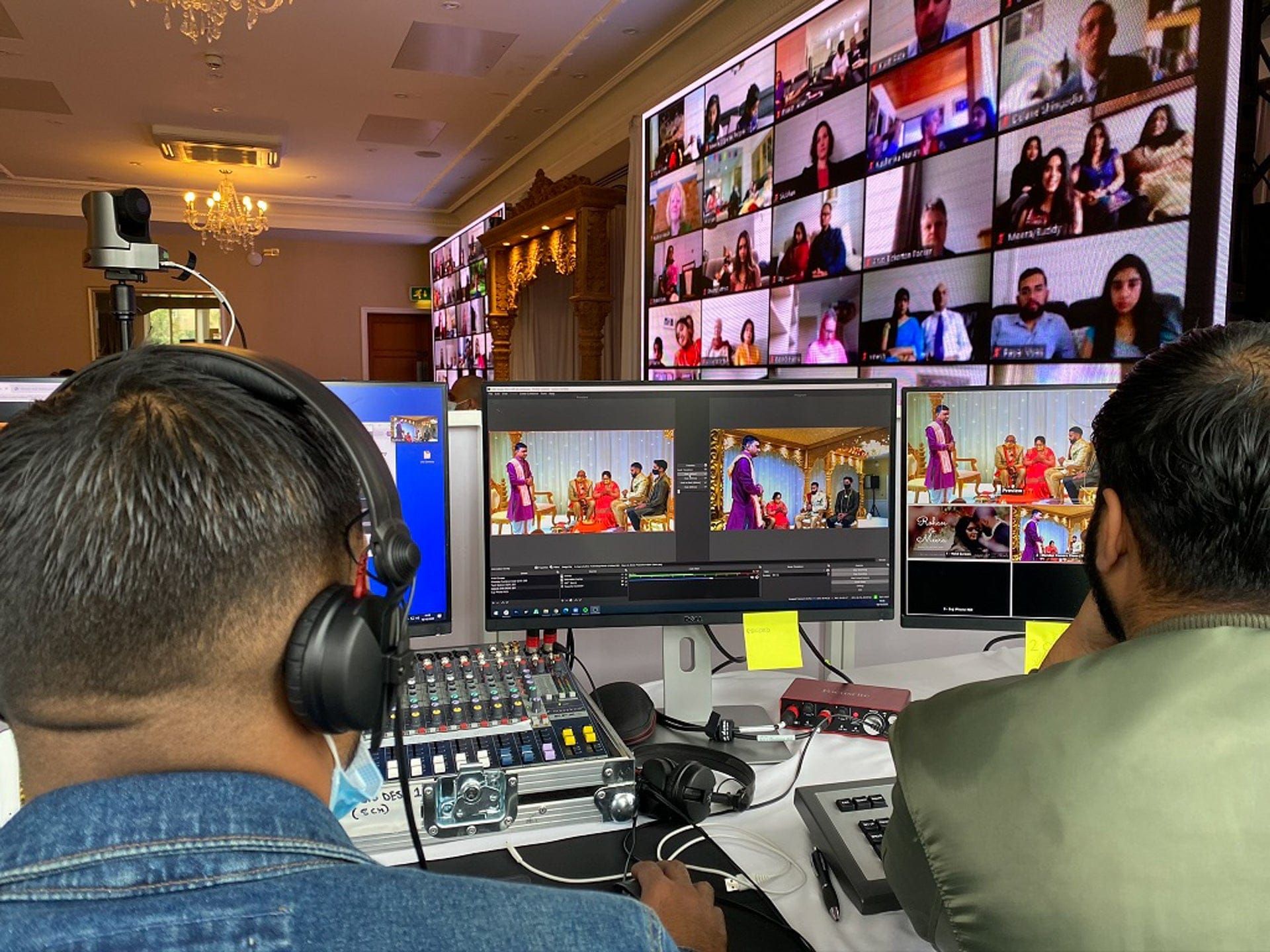 An engineer at a mixing desk watching a multi-camera feed and a grid of remote guests