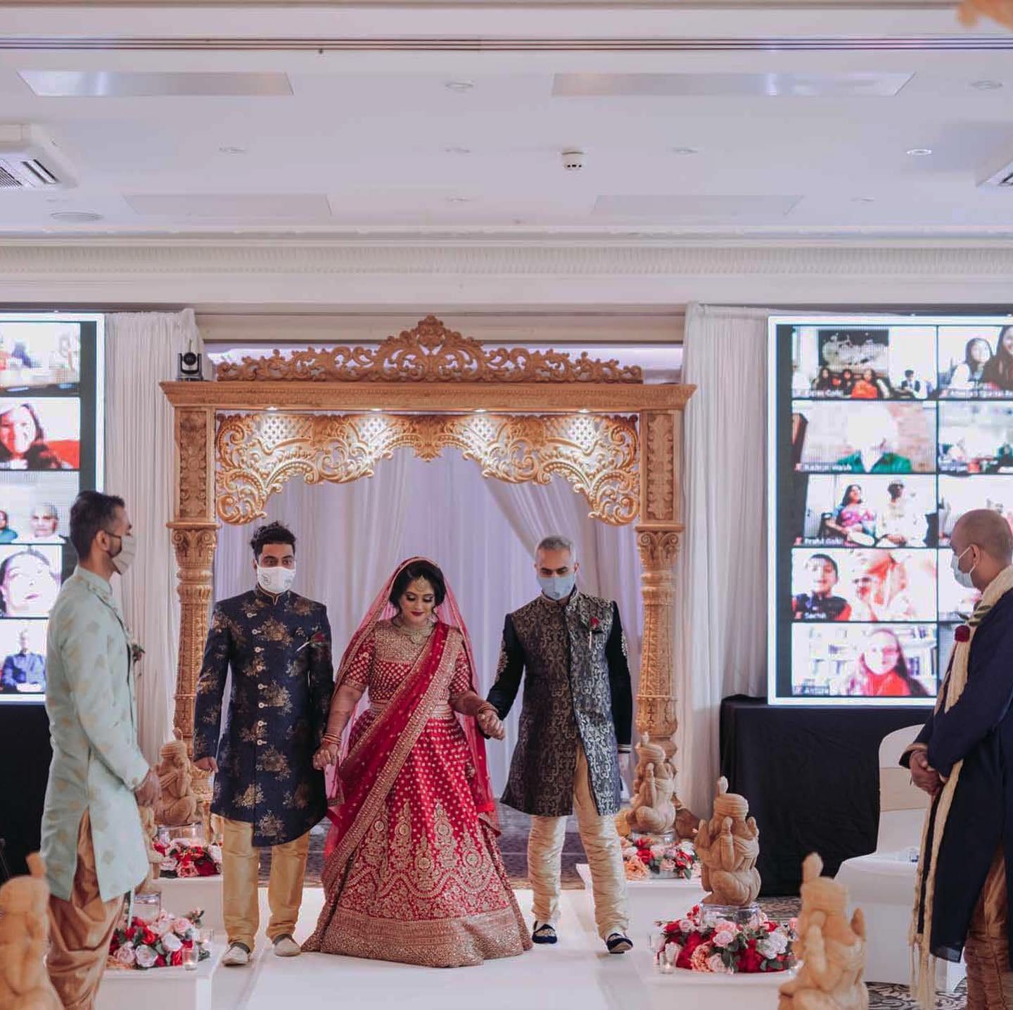 A wedding ceremony flanked by screens carrying a grid of remote guests