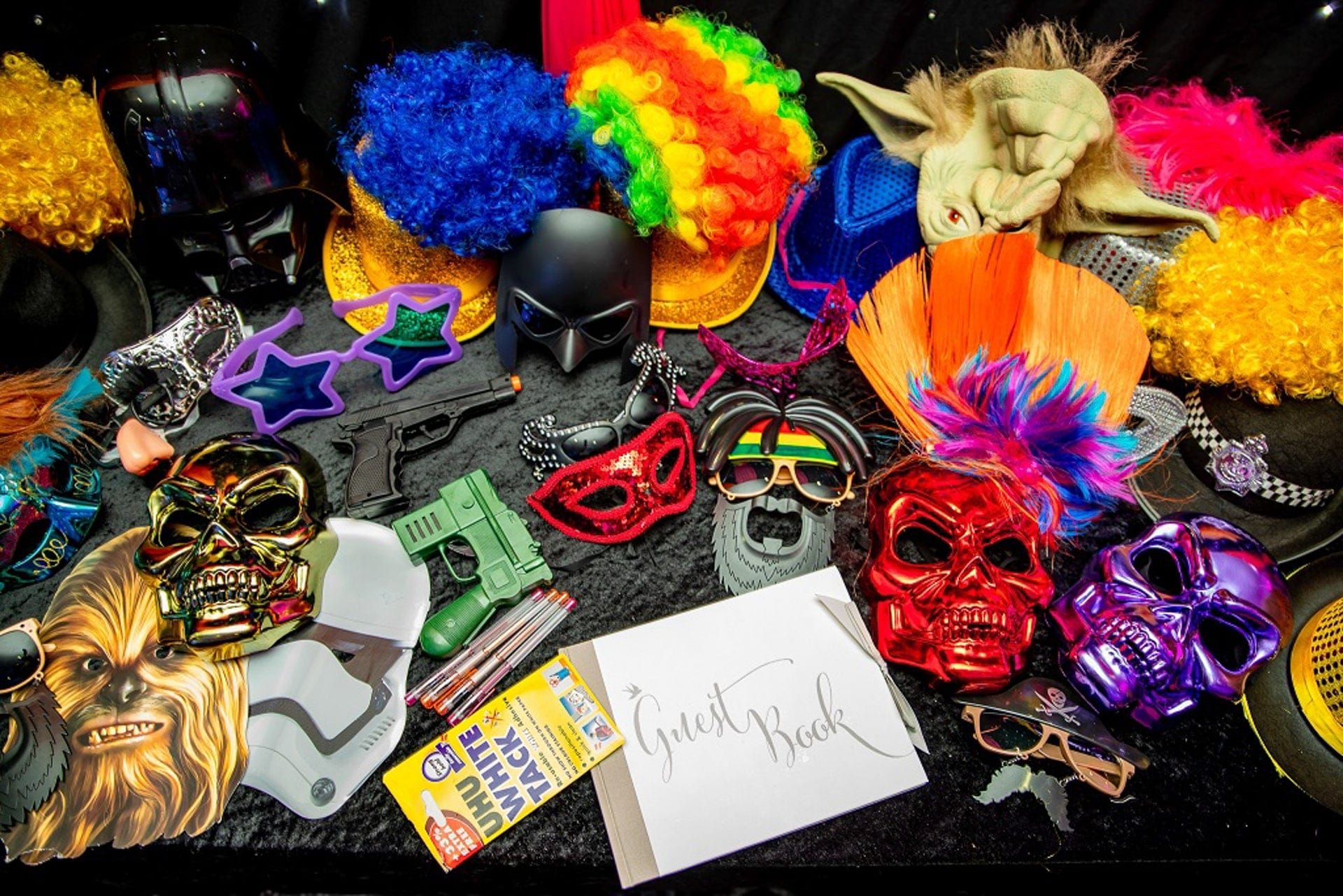 Photo booth props laid out: wigs, masks, novelty glasses and a guest book