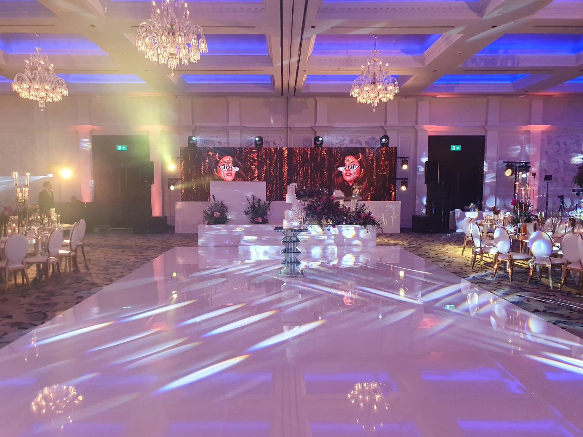 A white LED dancefloor under chandeliers, the room washed blue and violet