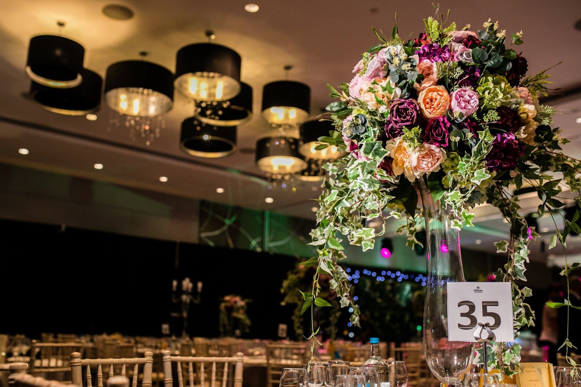A tall glass centrepiece of garden roses and trailing ivy above a set dinner table