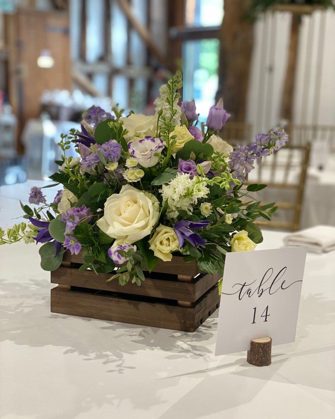 A low arrangement of white roses and lisianthus in a wooden crate beside a table number
