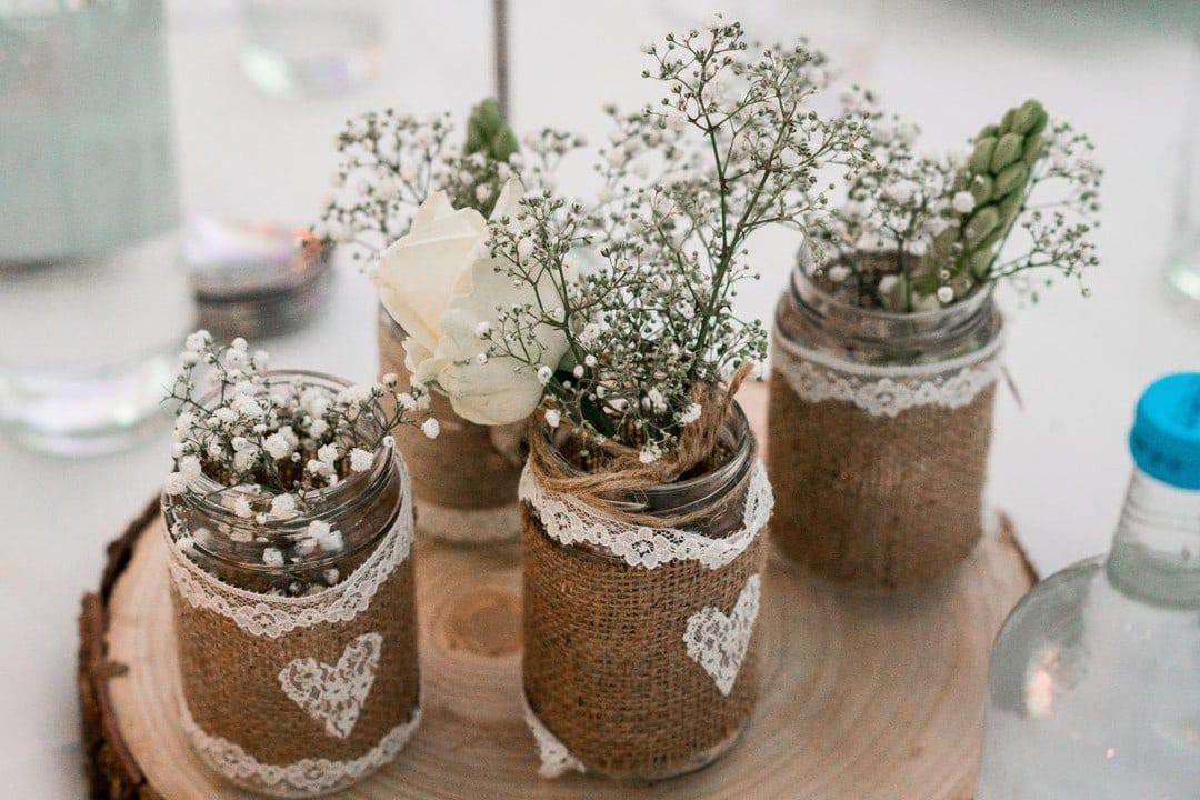 Jars wrapped in hessian and lace holding gypsophila, grouped on a wood slice