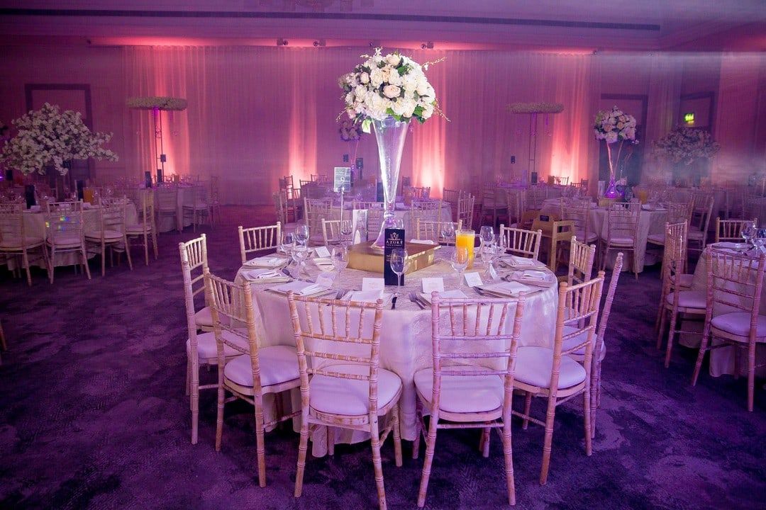 Round tables under tall floral stands in a room lit pink and violet