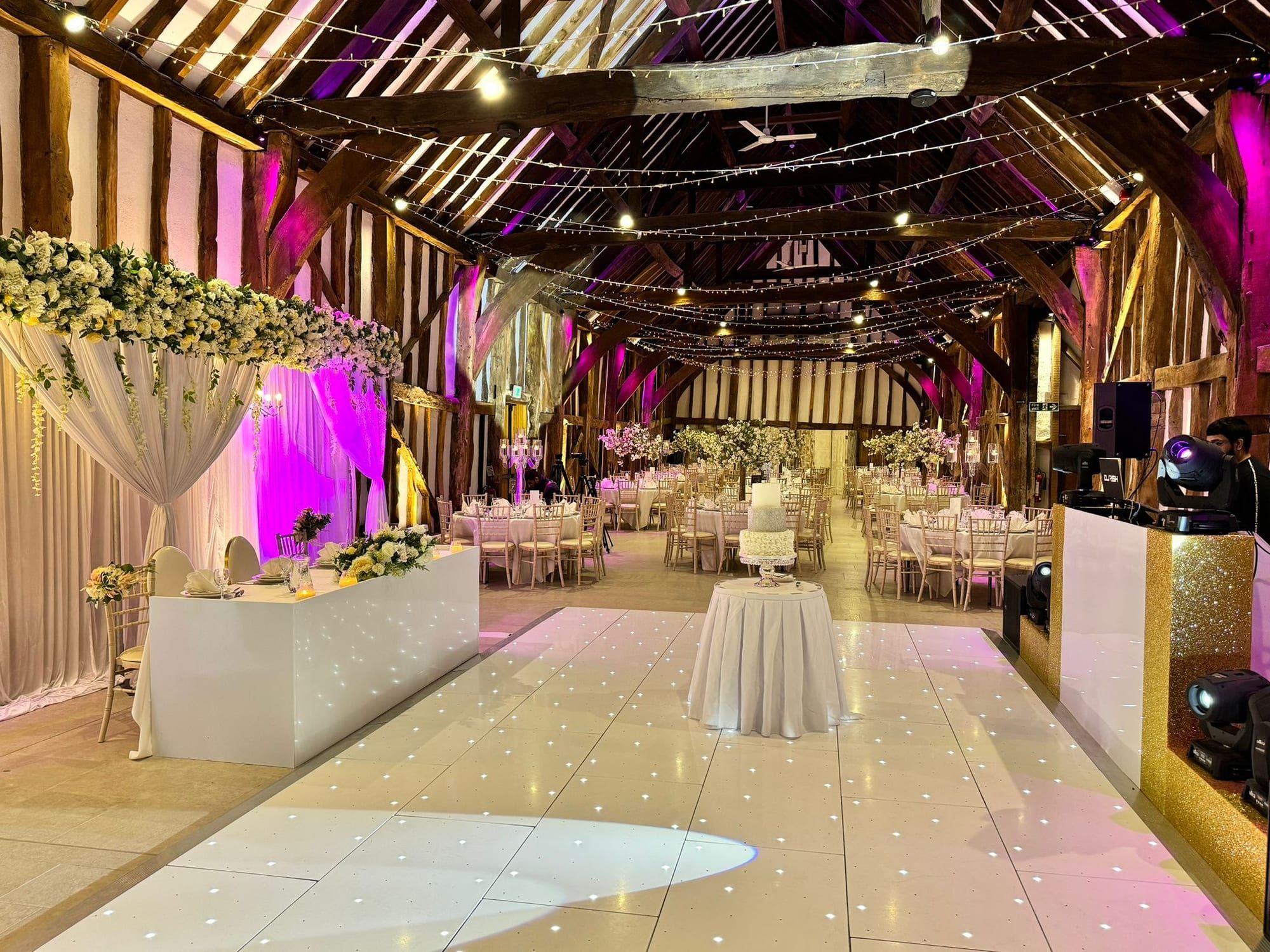 The Great Barn set for a reception, white dancefloor and pink uplighting along the walls