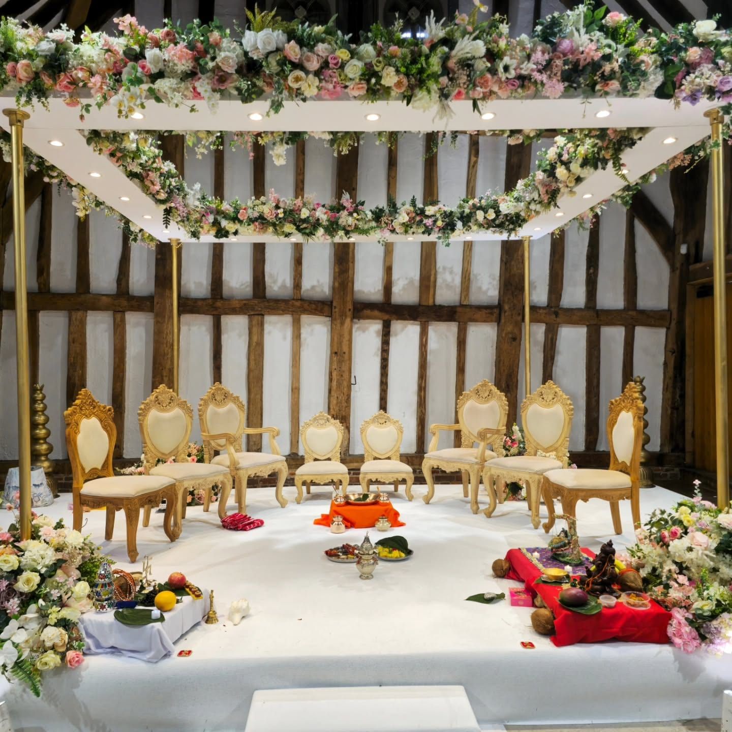 Gold chairs on a white stage beneath a garland-hung beam in the Great Barn