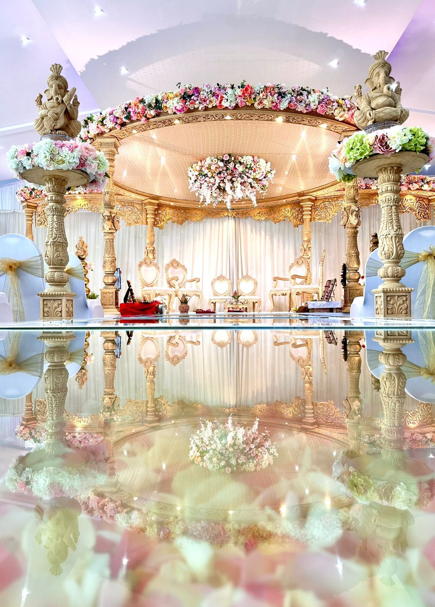 A gold pillared mandap reflected in a mirrored floor beneath chandeliers