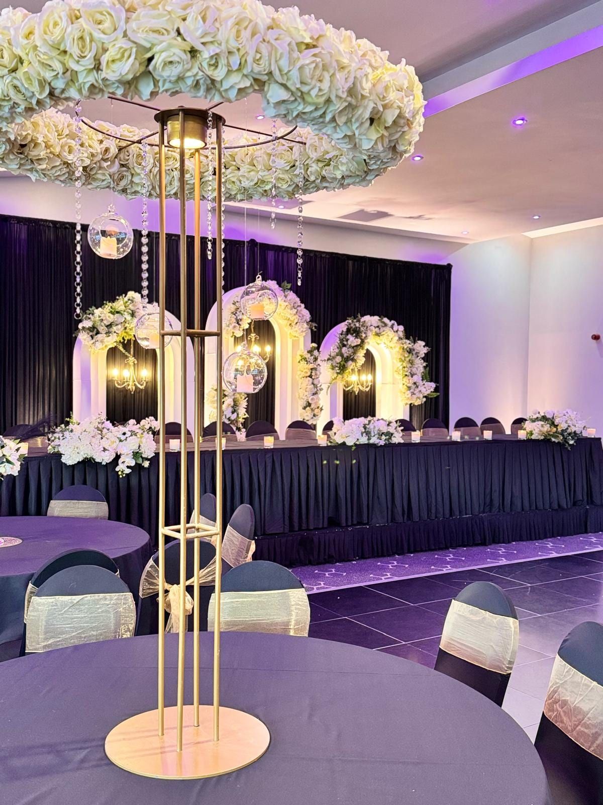 Floral arches and a draped top table in a room lit purple