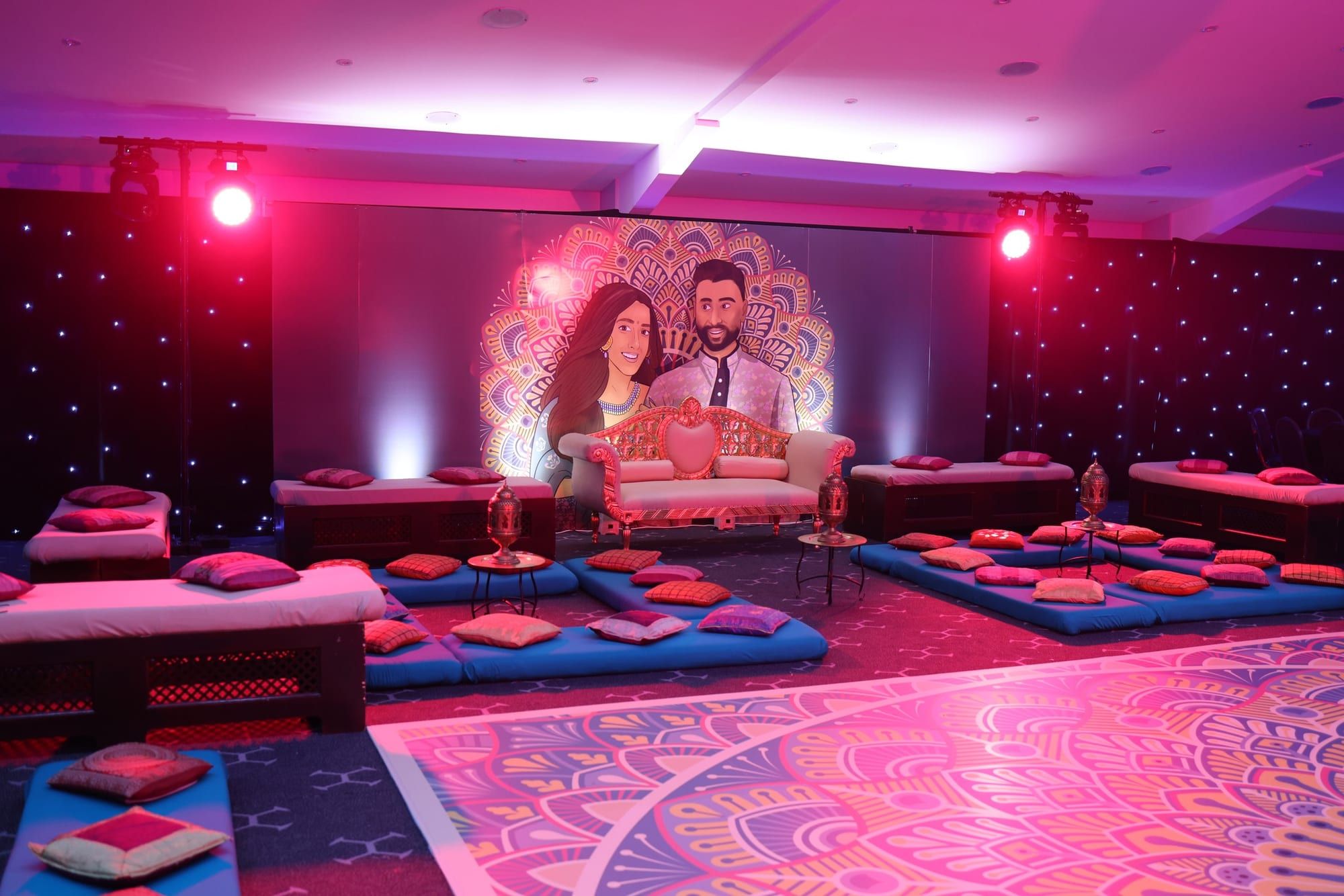A mehndi setting of low seating and floor cushions on a printed pink floor