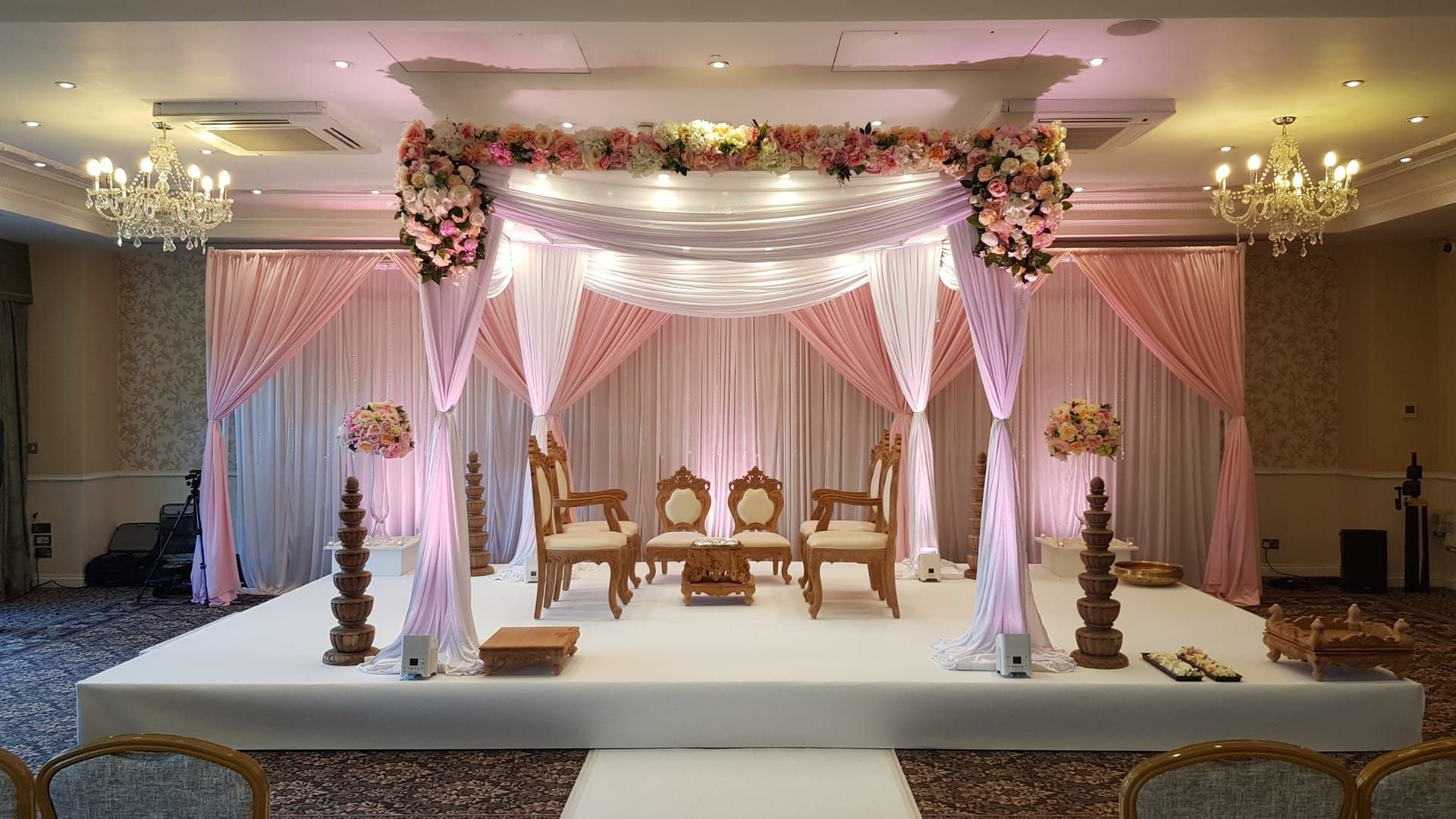 A ceremony canopy draped in soft pink and white silk beneath a floral surround