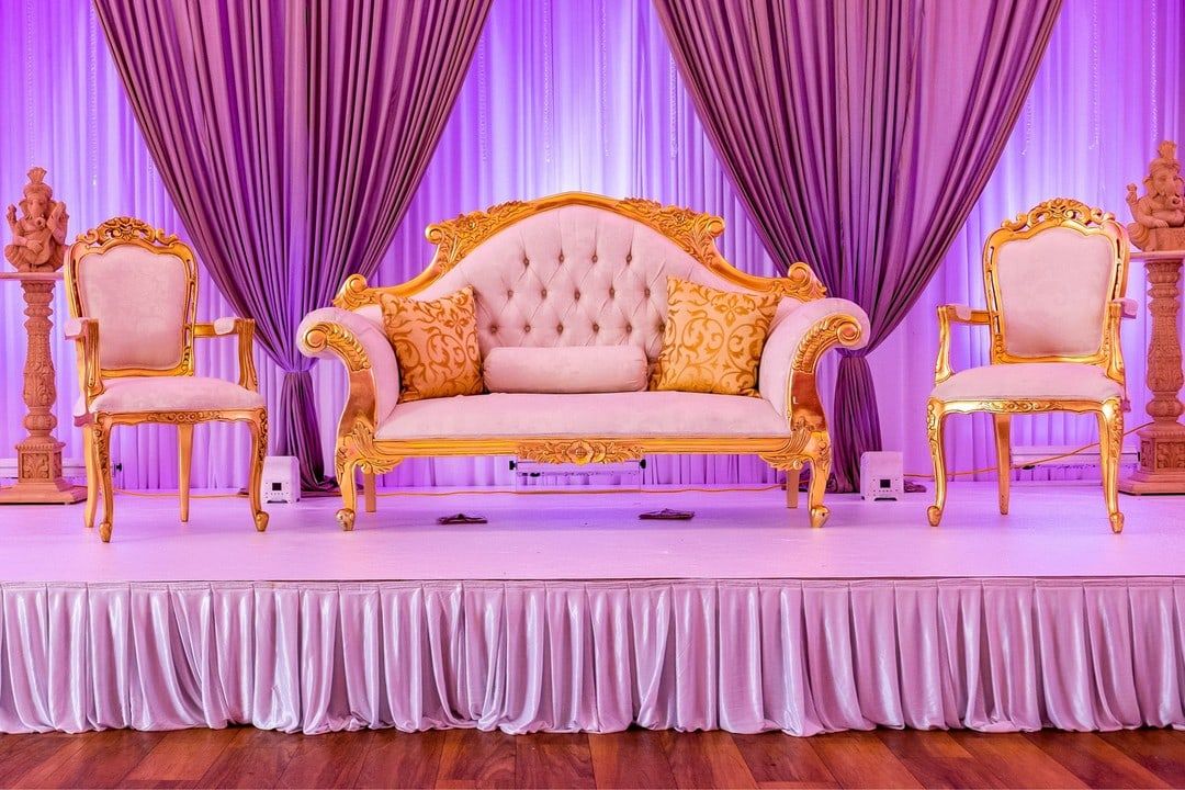 A stage backed by gathered pink drapes, gold framed seating on a skirted platform