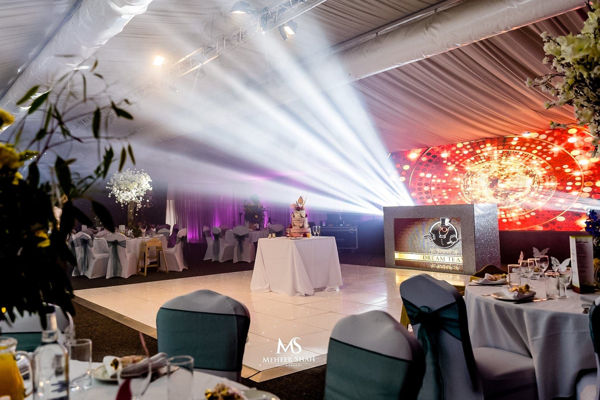 A wedding reception with a tiered cake, teal chair sashes and beams of light across the room