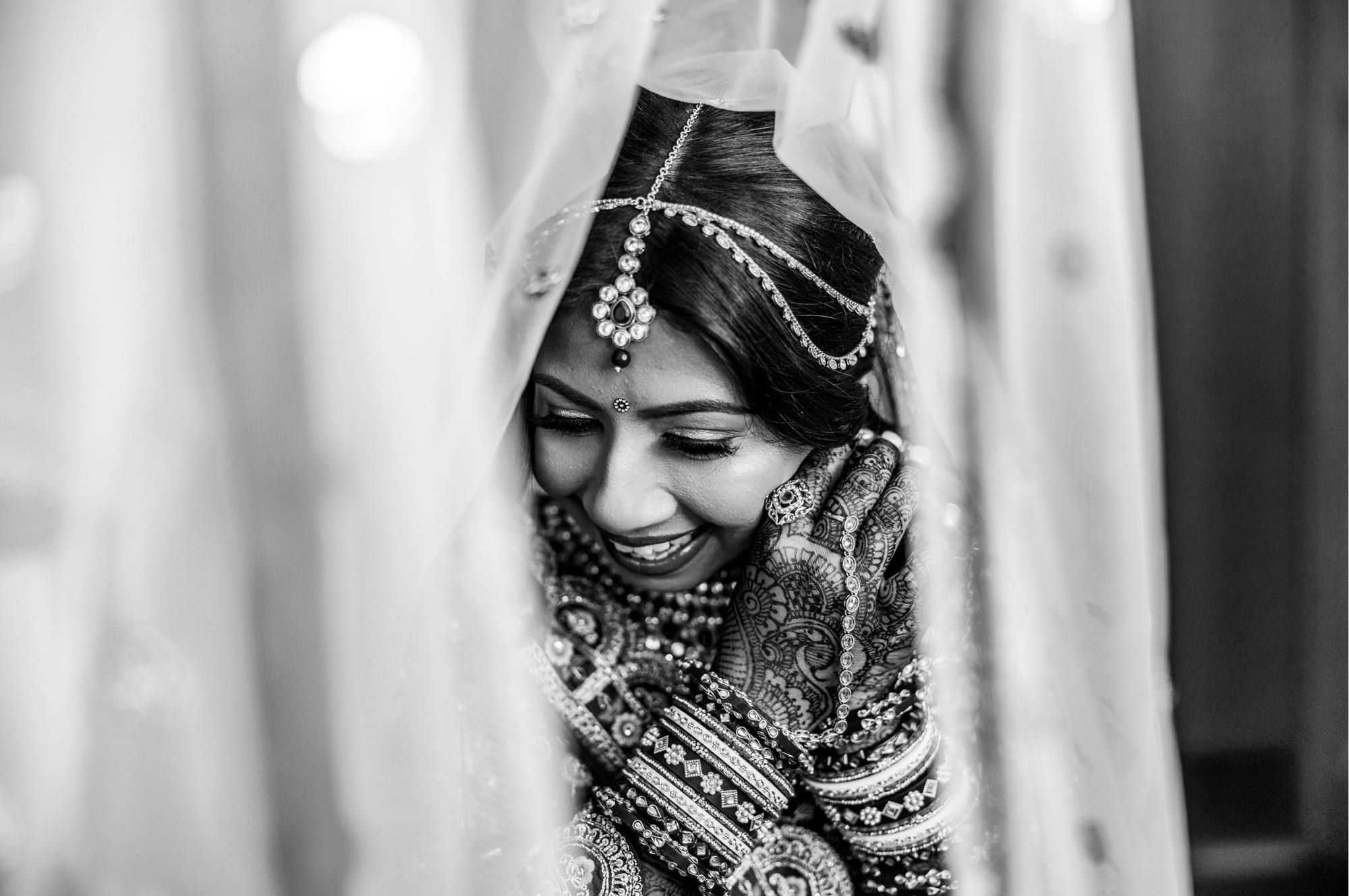 A bride in bridal jewellery photographed in black and white through a veil