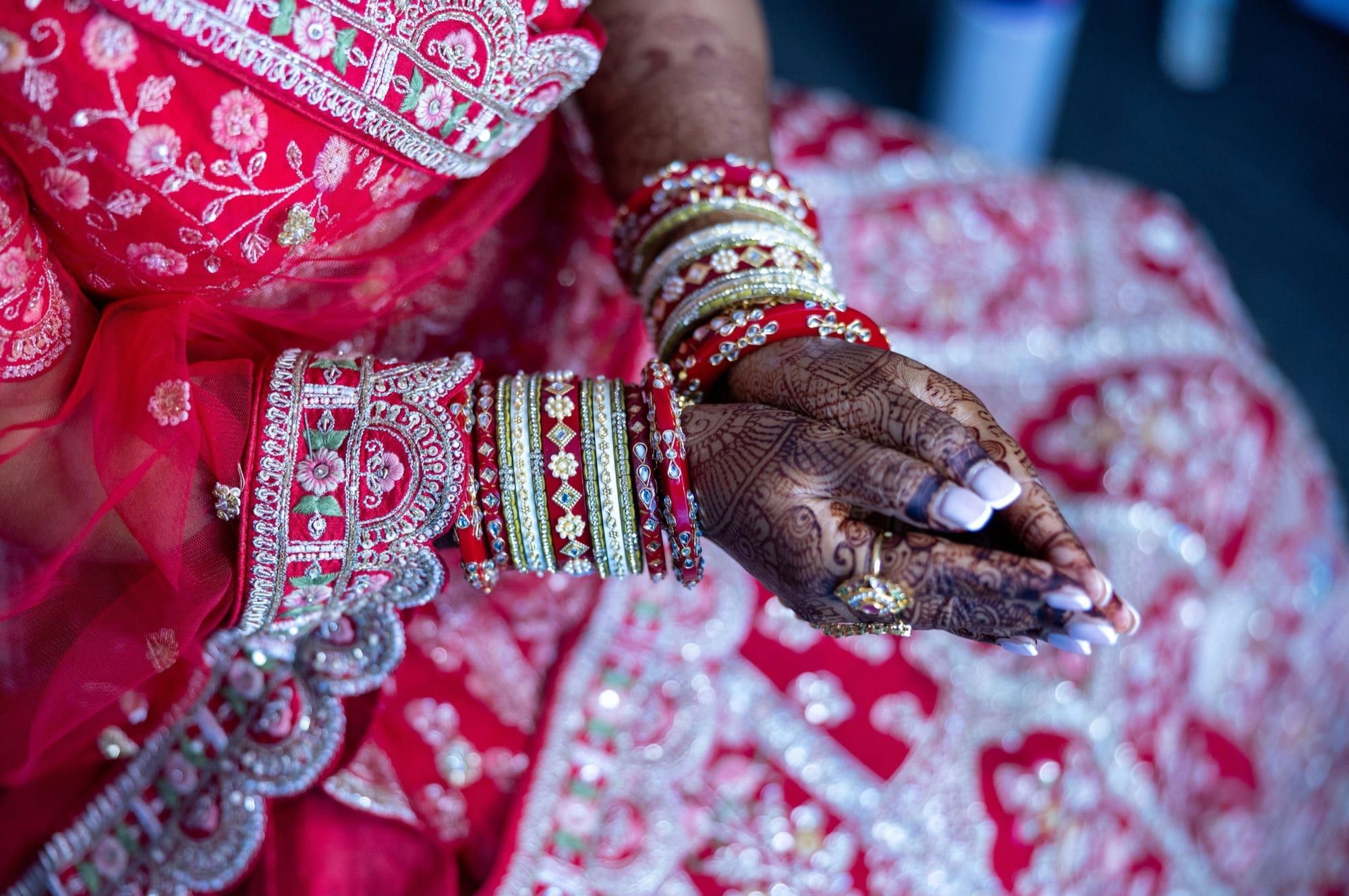 A bride's hennaed hands resting on a red and gold lehenga